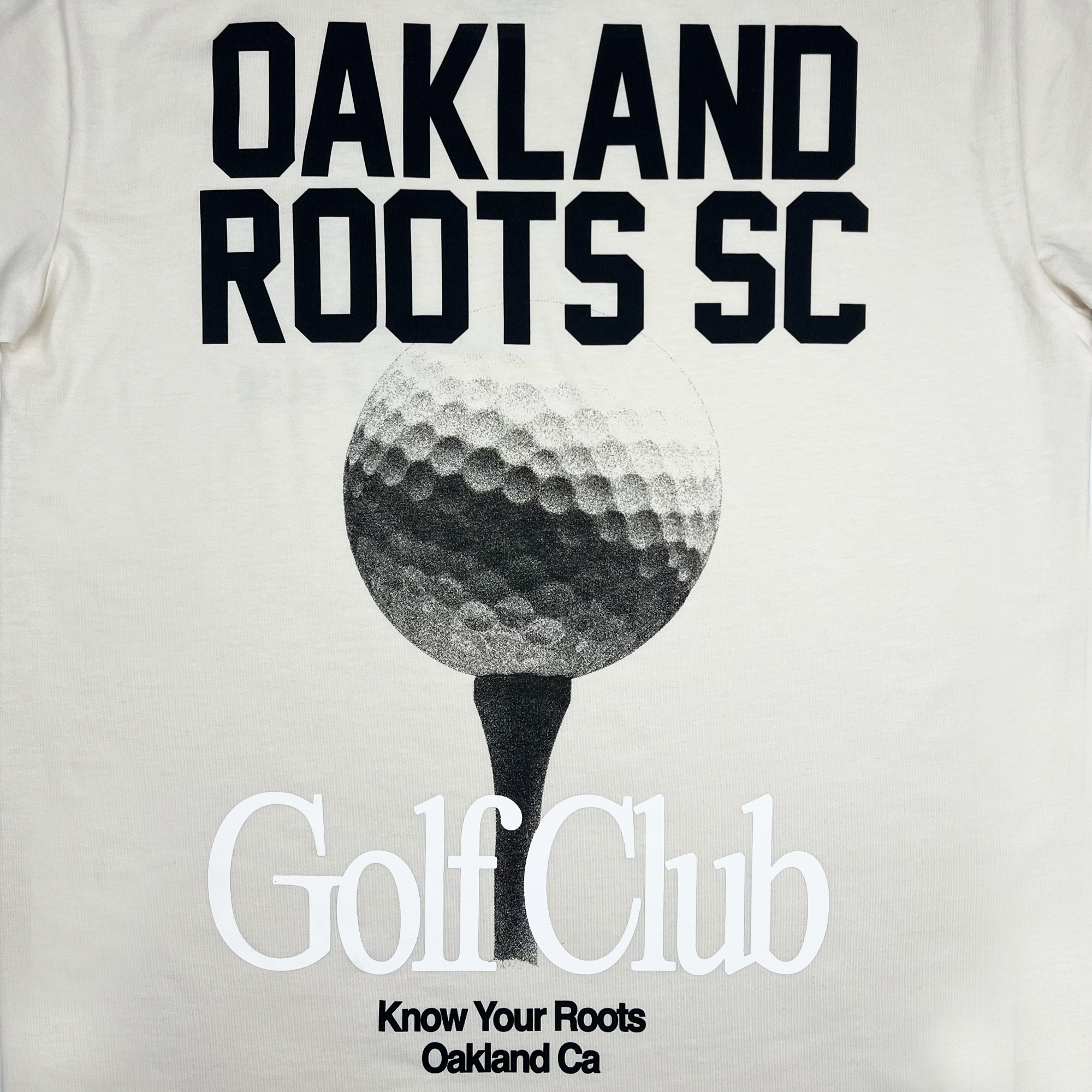 A white shirt design from Oakland Roots SC, showcasing the text "OAKLAND ROOTS SC" in bold, black letters at the top. Below, there's a large image of a golf ball on a tee with the words "Golf Club" in elegant, white text. At the bottom, smaller text reads "Know Your Roots Oakland CA," reflecting our commitment to social good.