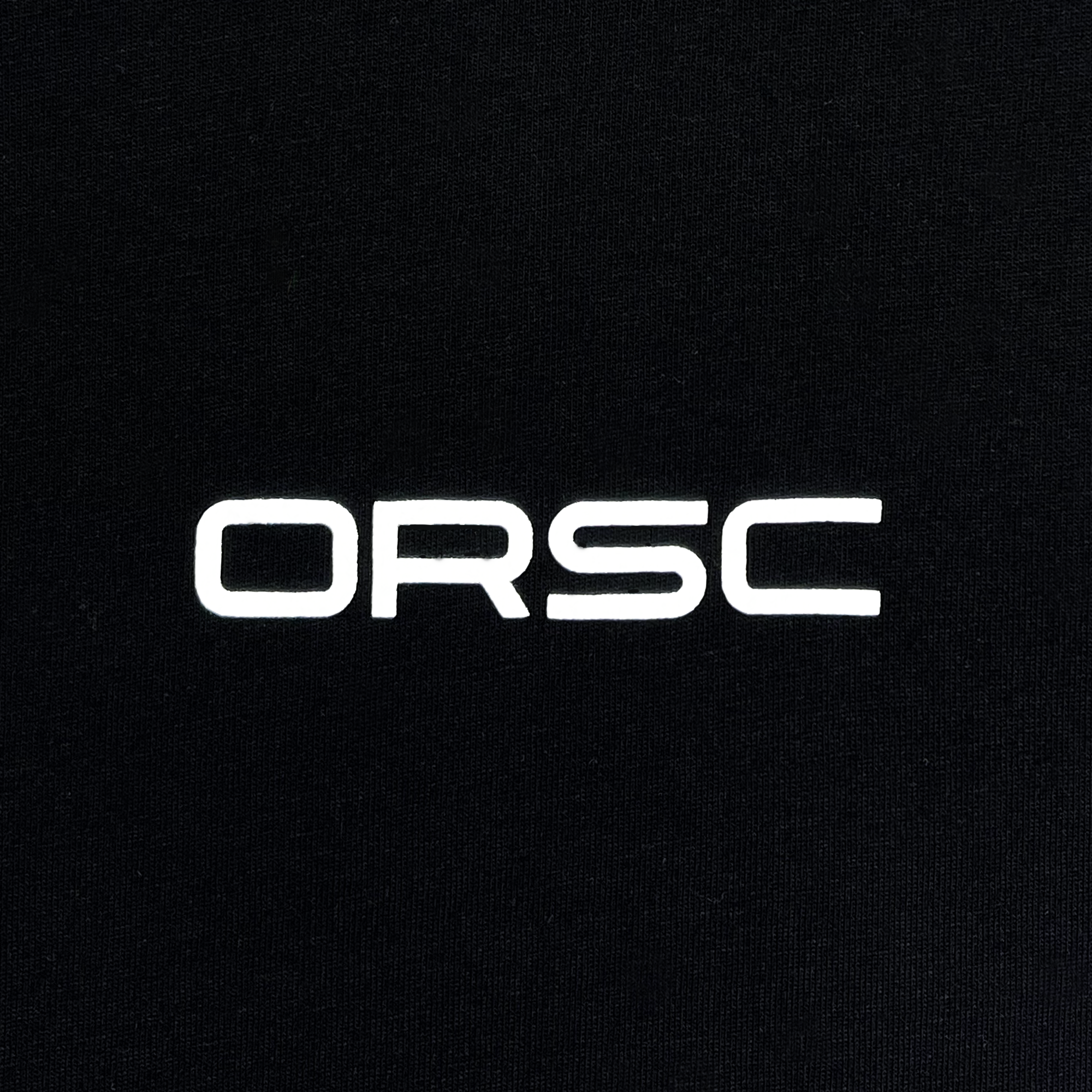 A black background with the white uppercase text "ORSC" prominently displayed in the center. The modern, sans-serif font creates a clean and minimalist design that embodies the spirit of social good at the heart of Oakland Roots SC, as seen on their Foundations Golf Tee.