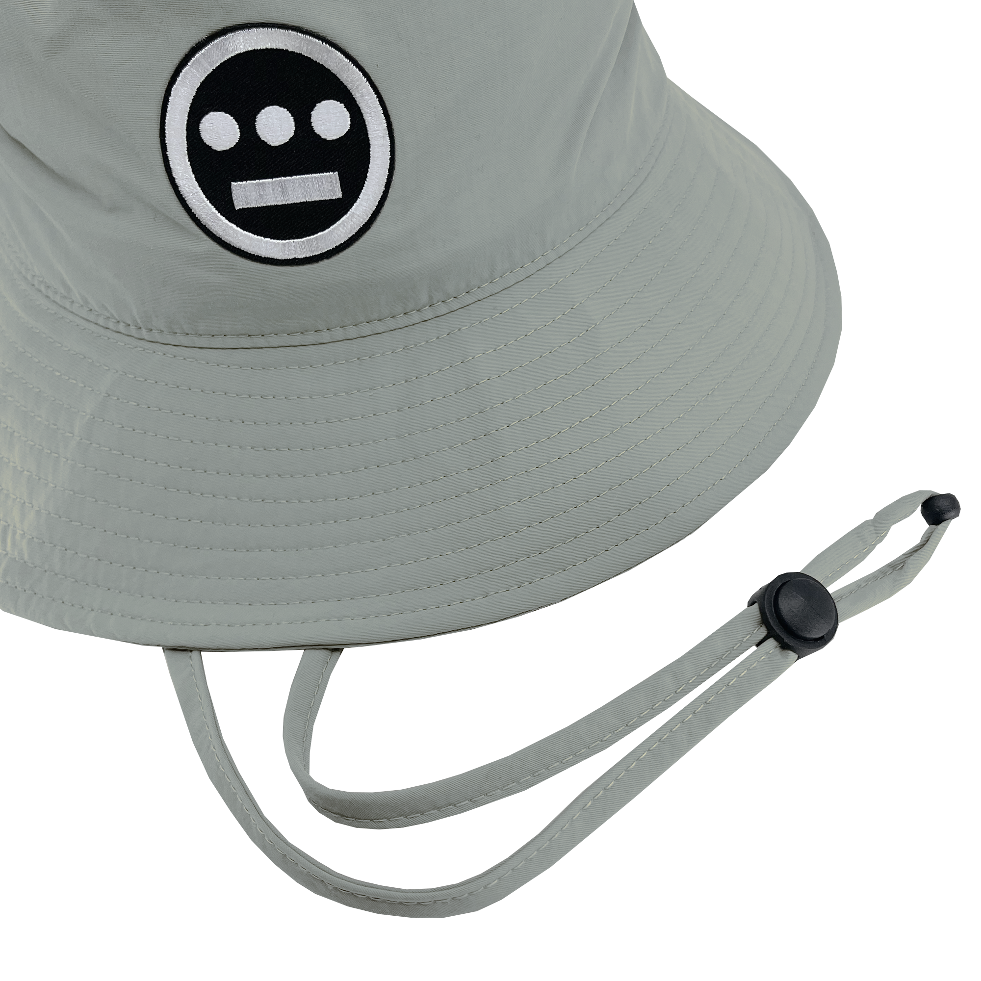 The Hieroglyphics Hiero Boonie Hat is a light gray bucket hat made from recycled nylon, showcasing a black and white embroidered logo of a circular face with two horizontal lines for eyes and one for a mouth. It features a chin strap and an adjustable black plastic toggle, merging style with sustainability as an eco-friendly accessory.