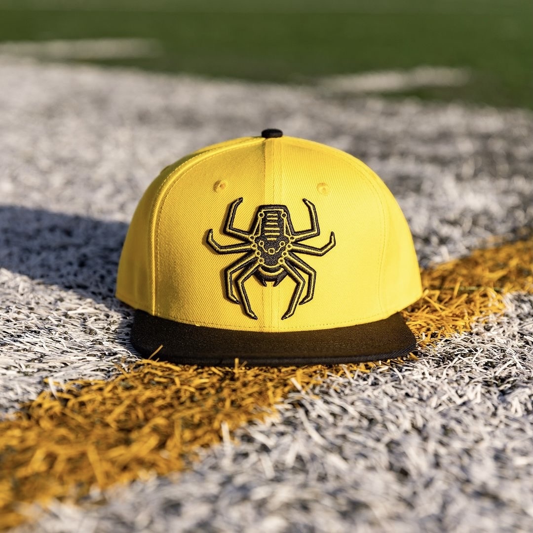 Yellow Spiders snapback on the field on a sunny day.