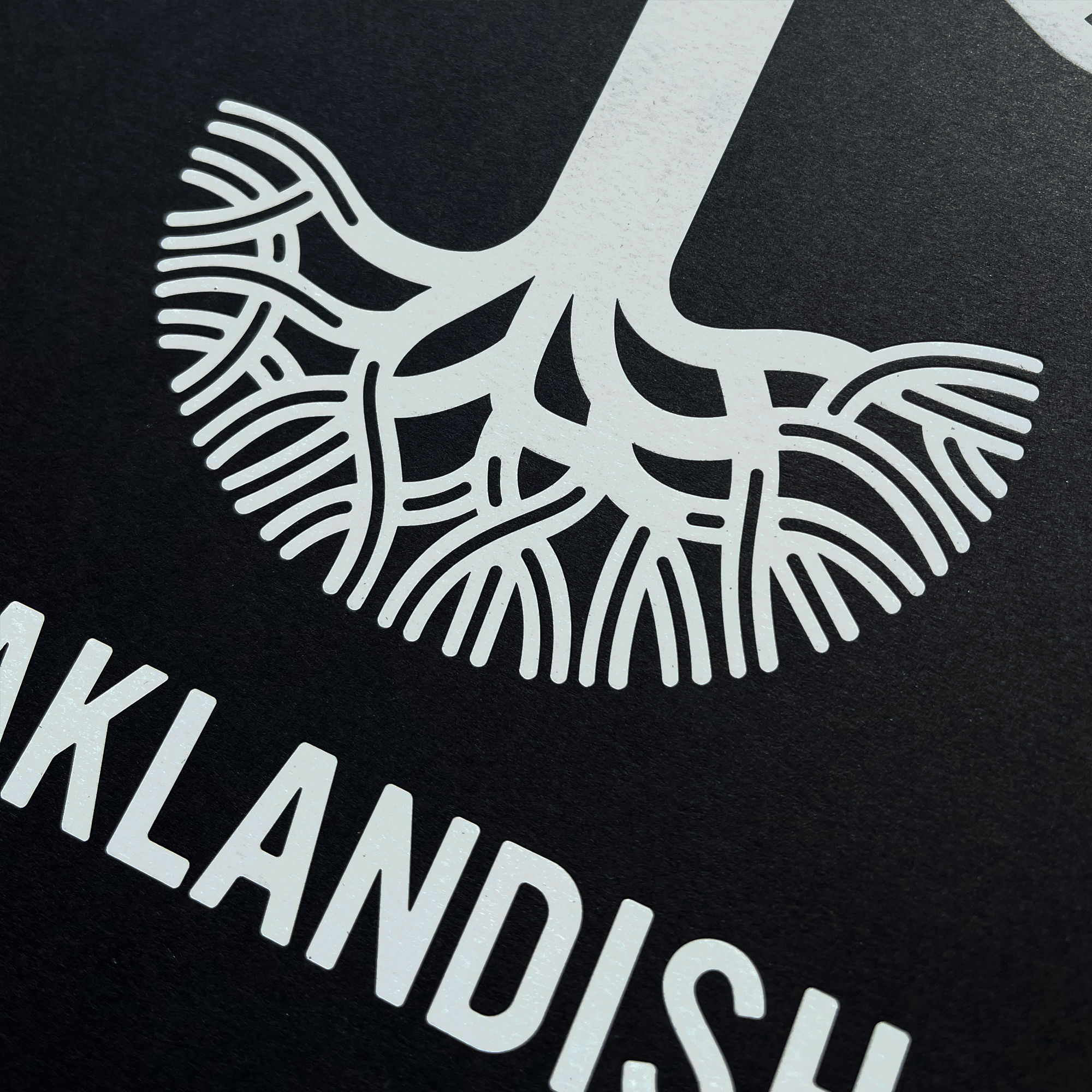 The Oaklandish New Logo Print by Never Elsewhere is a minimalistic and modern black poster showcasing a detailed white graphic of an intricate root system ending in numerous branches, all supported by a thin vertical line resembling a tree trunk. Beneath the graphic, bold white uppercase text reads "OAKLANDISH," crafted in the style of a detailed letterpress print.