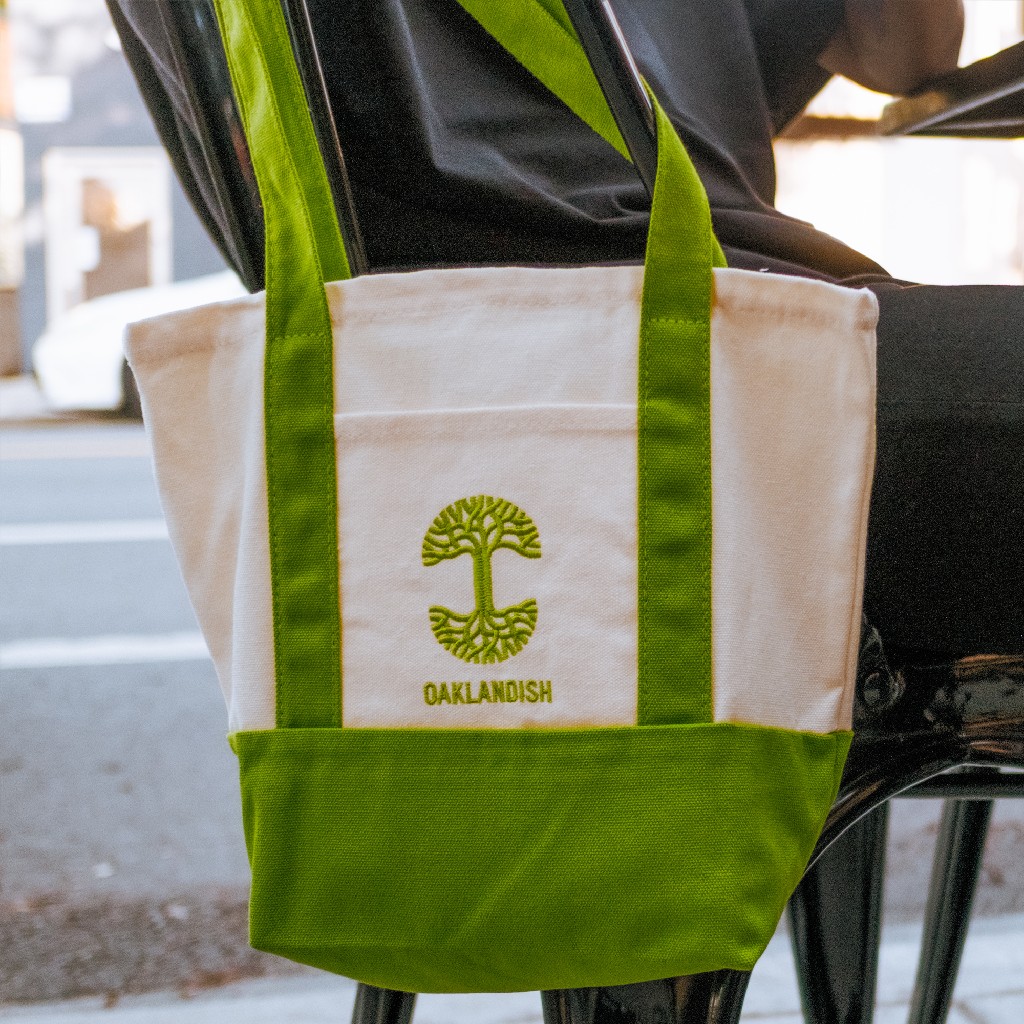 The Oaklandish Mini Grocery Tote by Oaklandish features green handles, a green bottom, and an embroidered tree logo with "OAKLANDISH" on the front—a stylish canvas bag perfect for everyday use.