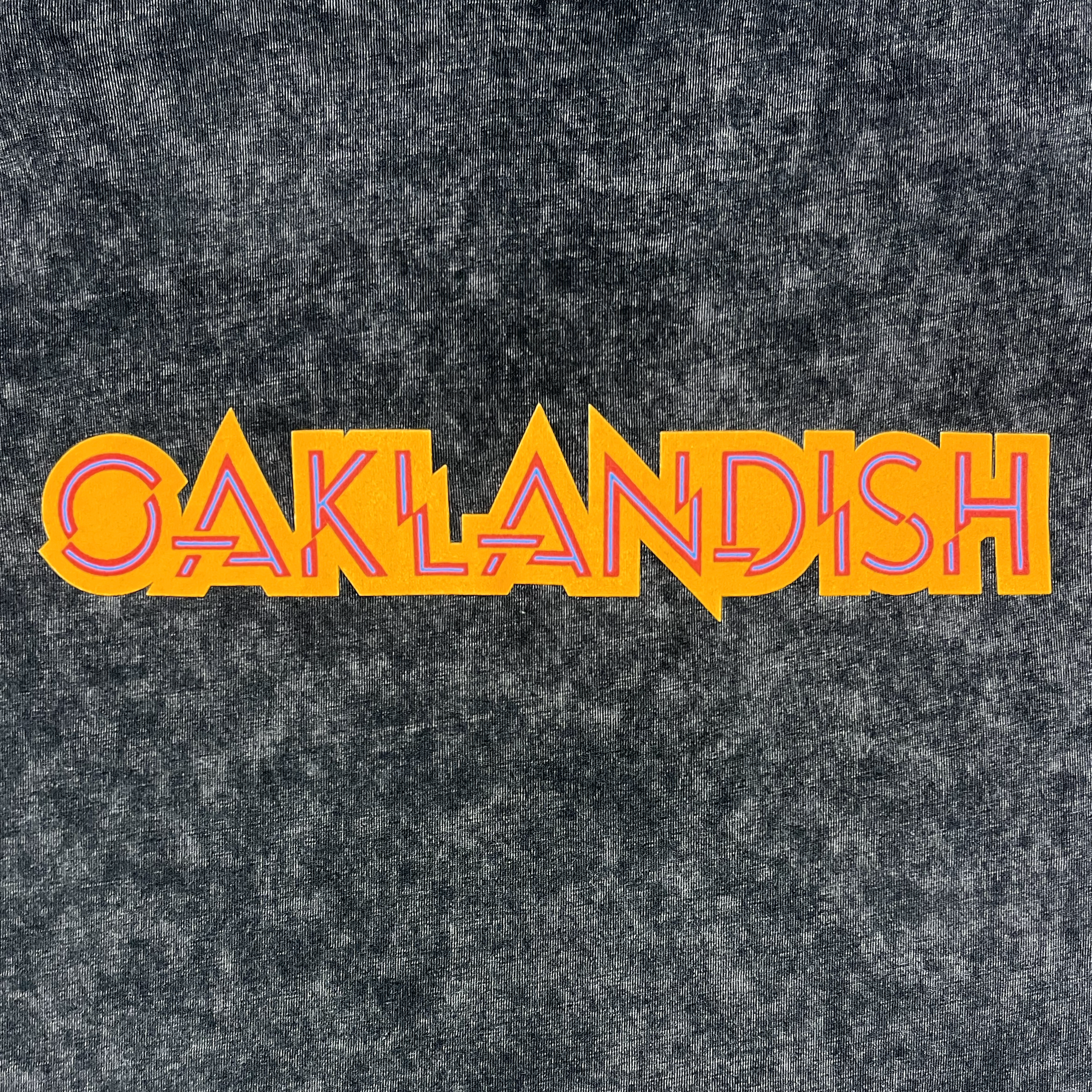 Detailed view of black stone cotton t-shirt with Oaklandish wordmark in orange,  blue, and red.