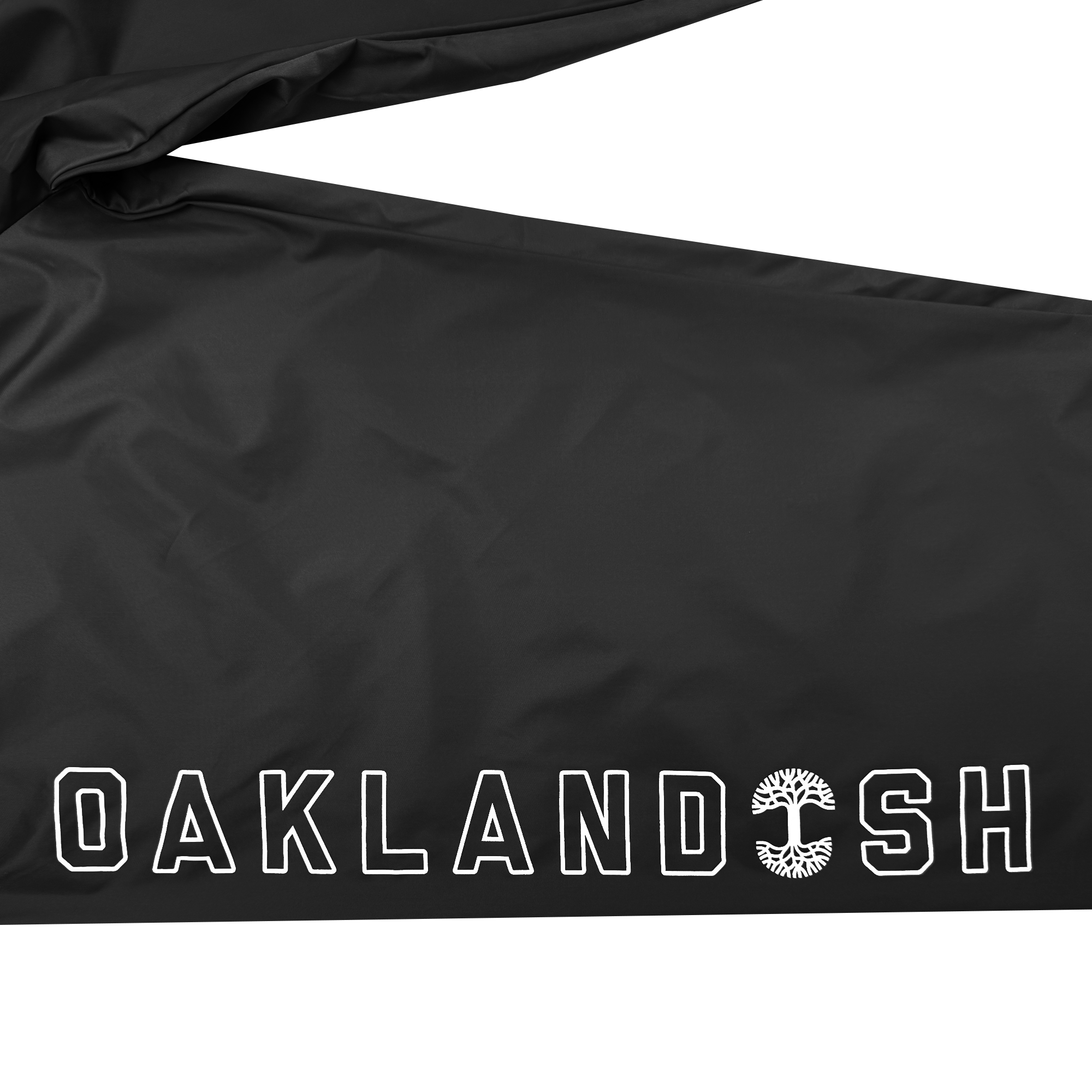 The Bandit Nylon Pant by Oaklandish showcases a glossy black fabric featuring the word "OAKLAND" in bold white letters, with the "O" incorporating an intricate tree design. These pants offer ultimate comfort and style, potentially pairing well with an adjustable waistband and a baggy fit.