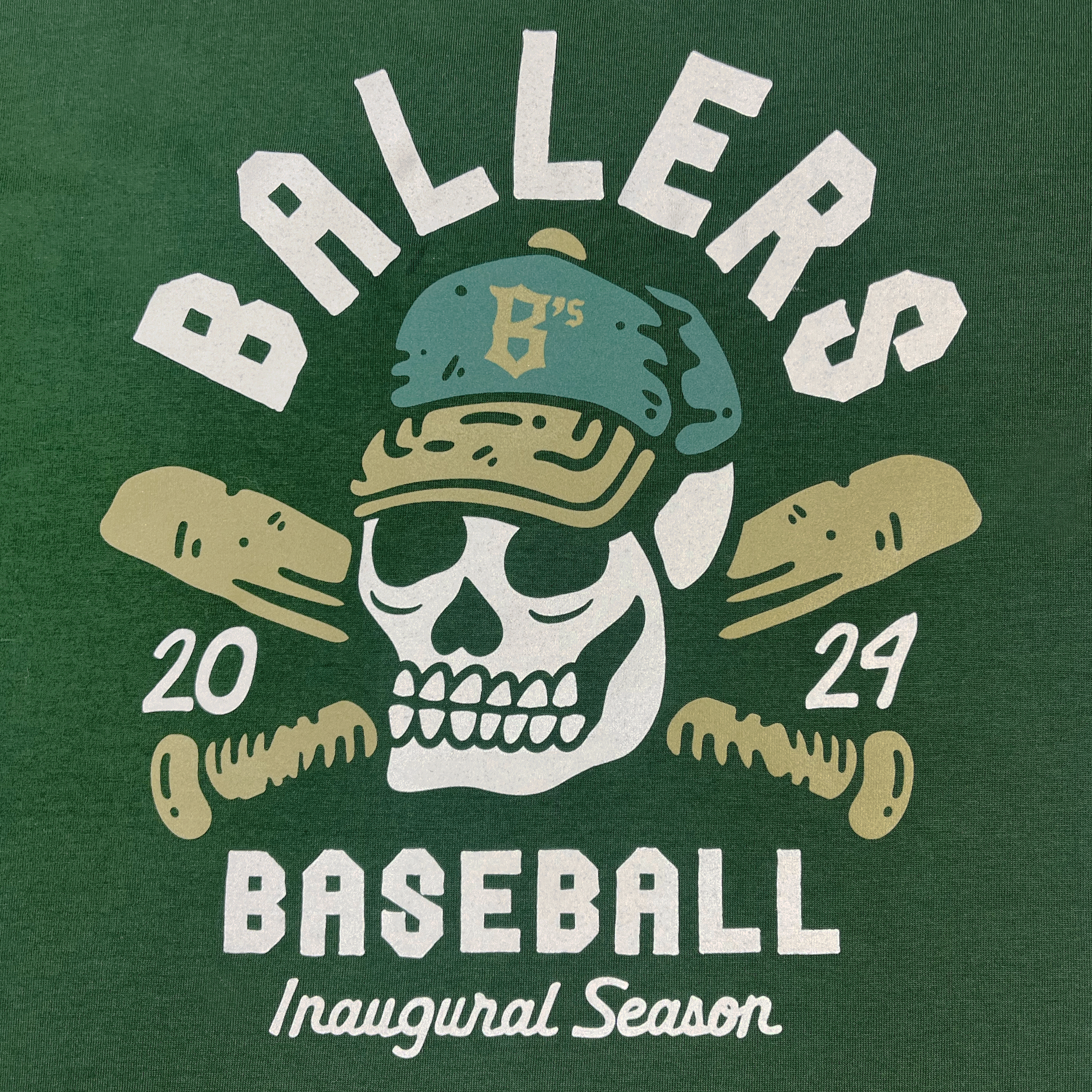 Description: The Oakland Til I Die Tee features a striking illustration on a green background. At the center is a skull wearing a baseball cap adorned with "B's." The skull is framed by two crossed baseball bats. Arched above the image is "BALLERS" and below it, "BASEBALL." To the sides are "2024," and at the bottom, it declares, "Inaugural Season of the Oakland Ballers, Pioneer League.