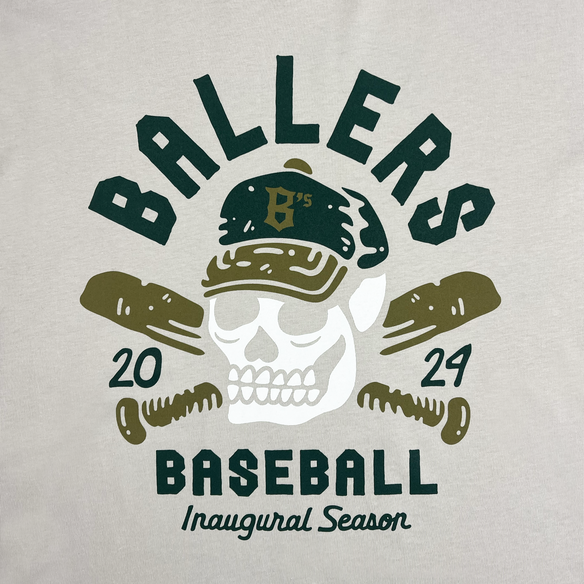 A vibrant graphic design for the Oakland Ballers' "Oakland Til I Die Tee" features a white skull wearing a green baseball cap marked with a yellow "B's." The word "BALLERS" arches above the skull, with "2024" flanking each side. Below, crossed baseball bats and the text "BASEBALL Inaugural Season" complete the design on a beige background, celebrating Oakland's new pro baseball team.