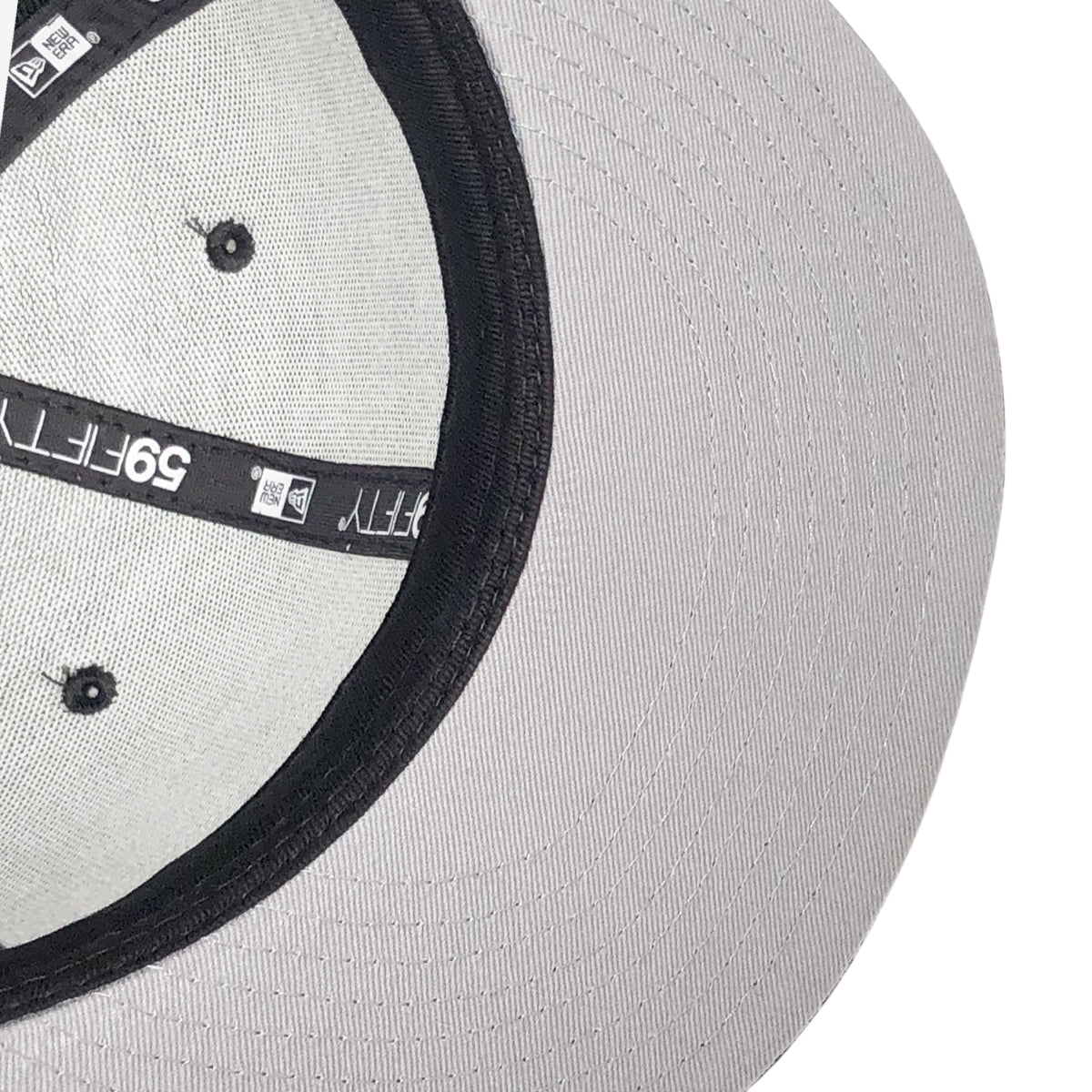 Close-up of the underside of a gray New Era OAK 59FIFTY Fitted Cap by Other, featuring black taped seams, visible stitching, black ventilation eyelets, and an interior “59FIFTY” logo label. The cap’s curved brim is partially visible in the background, with a hint of the OAK logo also on display.