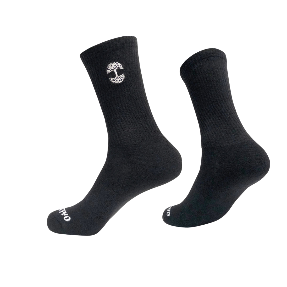 A pair of black crew socks, with one sock slightly elevated and angled to the side. The Embroidered Logo Socks feature a small, white, vertical emblem resembling a tree on the upper part and white text "OAKPO" near the toes. These Oaklandish socks come in adult sizes, boasting a ribbed texture on top and smooth finish below.