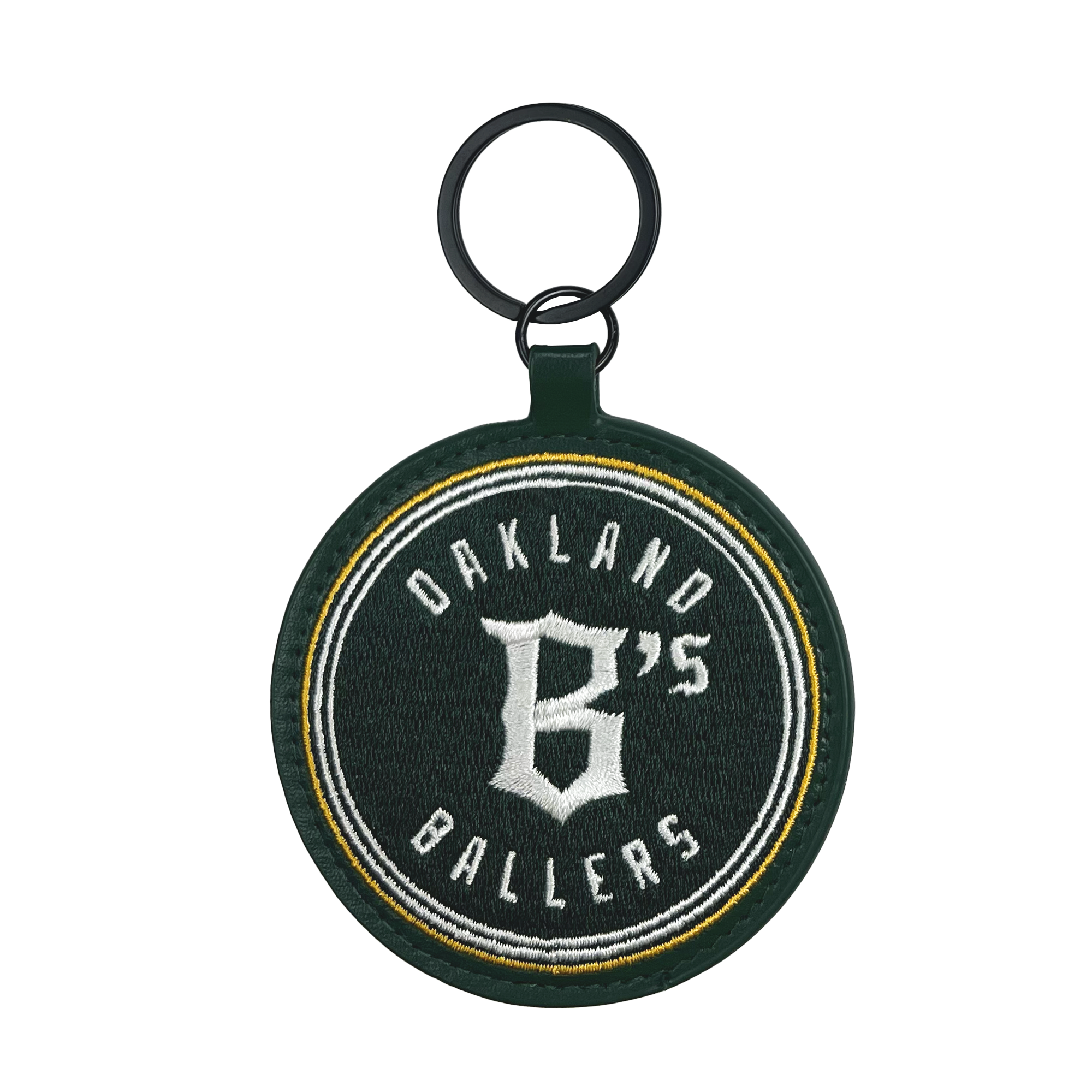 The Oakland Ballers Keychain features a round, dark green fabric embroidered with "Oakland Ballers" in white and a large "B's" at the center. It includes a black ring at the top for attaching keys and has a green border surrounding the entire design. The text is highlighted with yellow and white accent lines, celebrating this pioneering professional baseball team.