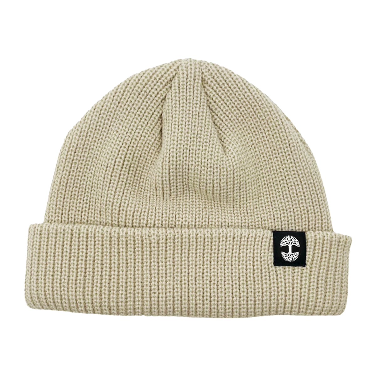 The Ramos Beanie by Oaklandish is depicted, showcasing headwear at its finest with its beige knit and folded brim. The brim features a distinctive black rectangular patch adorned with a white circular cross logo. Made from woven acrylic, the textured material likely provides warmth and comfort. The beanie boasts a simple, classic design that exudes timeless style.