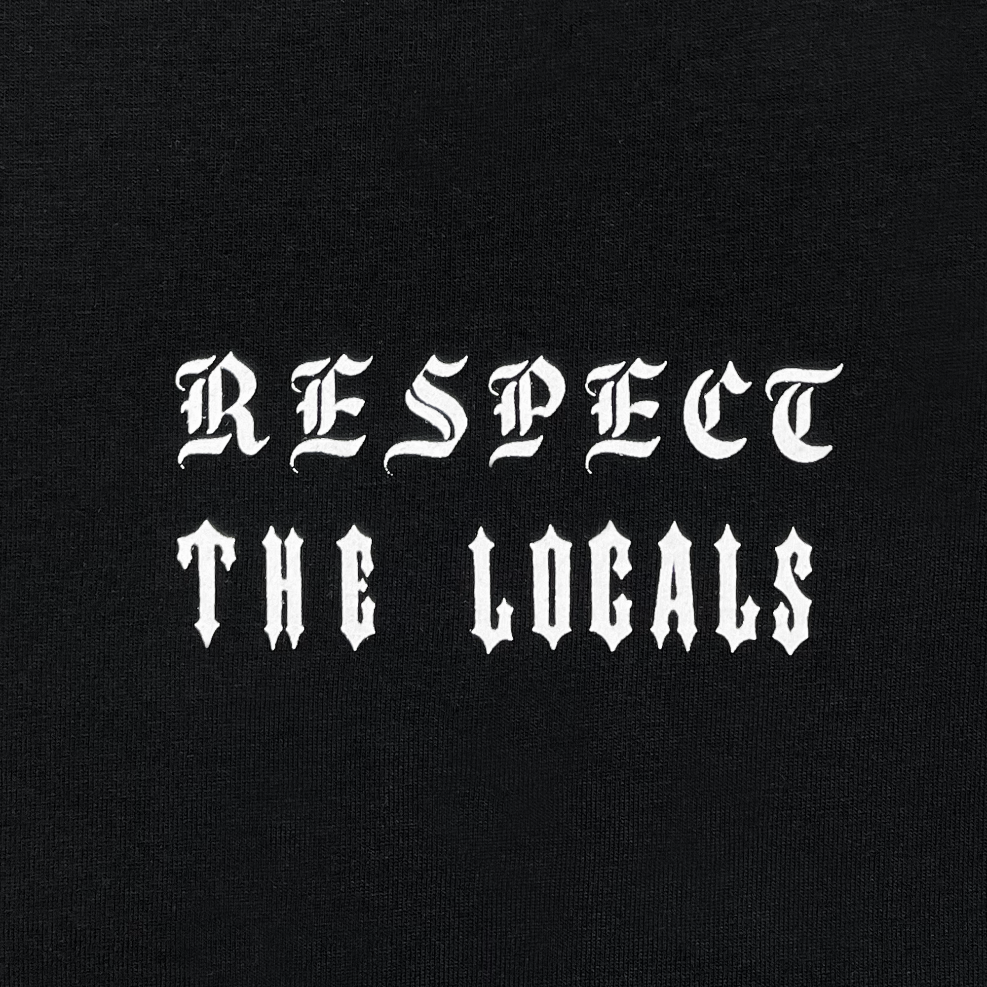 The image features the text "RESPECT THE LOCALS" in a gothic, old English-style white font on a solid black background. The bold and elaborate lettering, reminiscent of tattoo design, is prominently displayed on the Respect the Locals LS Tee by Oaklandish. Made from 100% cotton for a classic fit, this long sleeve t-shirt effectively conveys a clear and strong message.