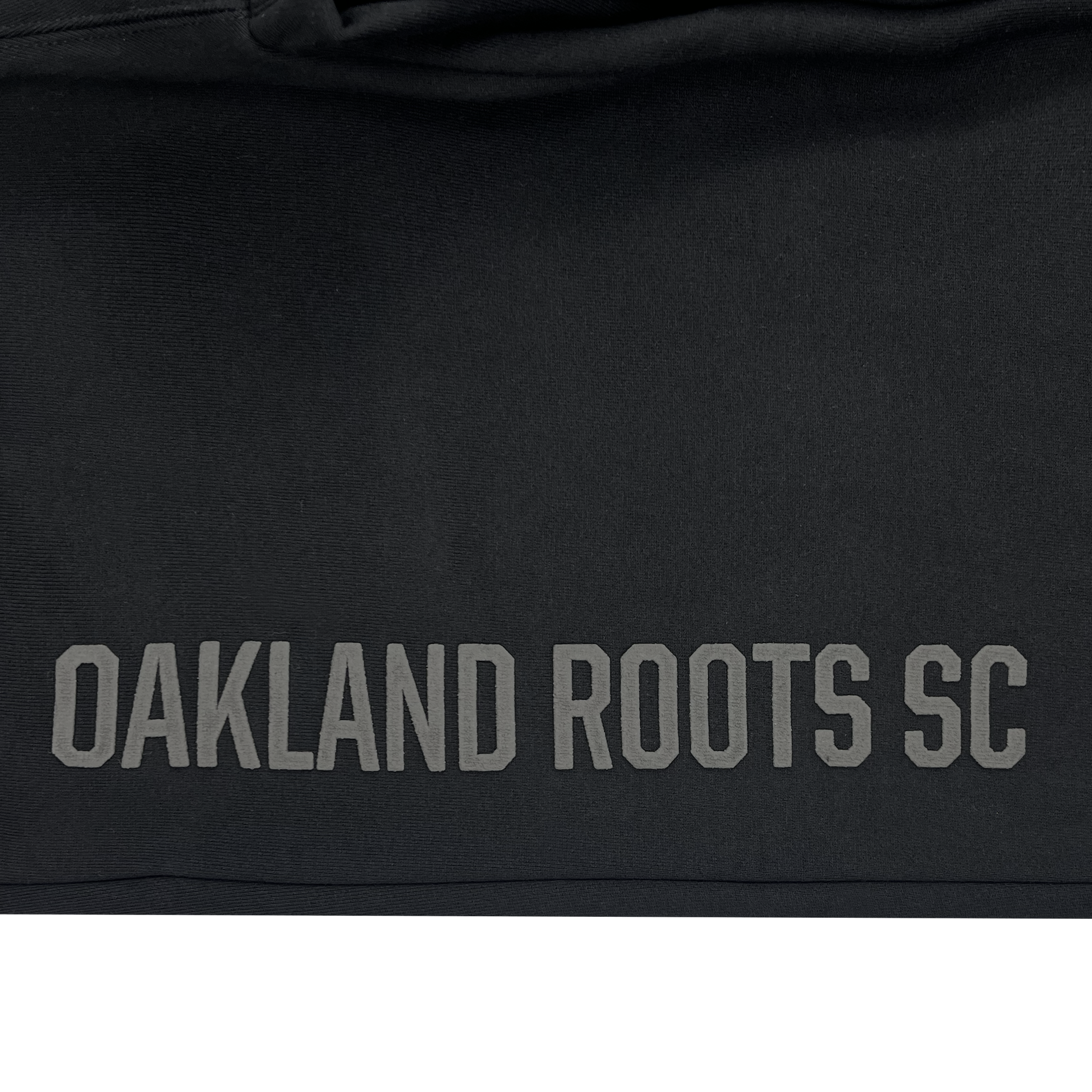 Detailed view of black cotton sweatpants with tonal imprints of Oakland Roots SC down right leg.