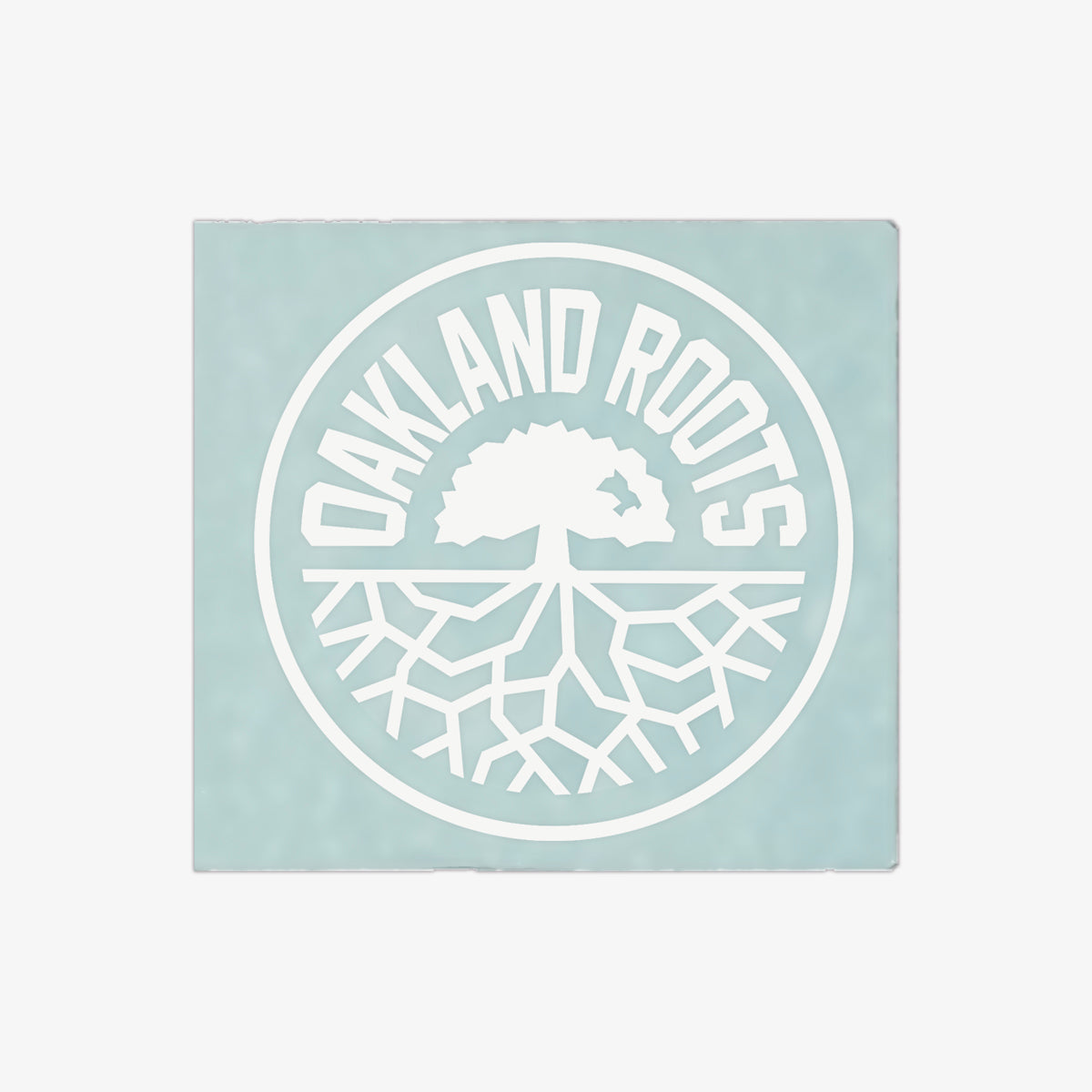 The Oakland Roots SC Decal - 6" features a pale blue-green background with a white circular logo. "OAKLAND ROOTS" is written in all caps along the top edge inside the circle, while a simplified tree with visible roots is centered within it, symbolizing Oakland Roots Sports Club's deep connection with its community. This decal is perfect for adorning your window!