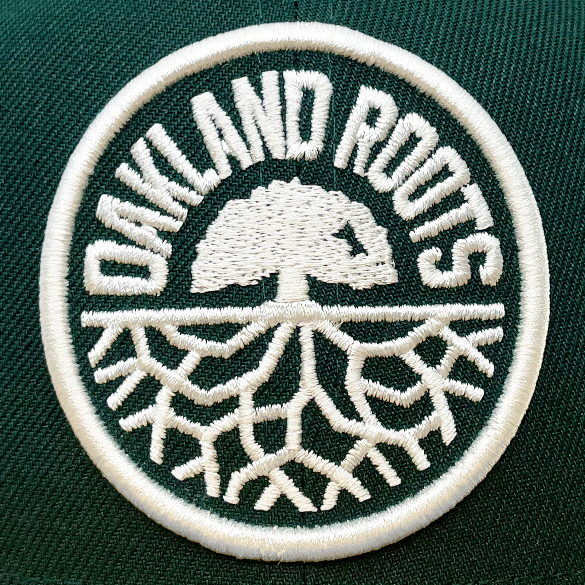 The New Era Oakland Roots SC 59FIFTY Cap showcases a circular patch with a green background, displaying the words "OAKLAND ROOTS" in white embroidery above a white tree with spreading roots. This design celebrates origins and growth, embodying the Oaklandish spirit. Ideal for any New Era cap enthusiast.