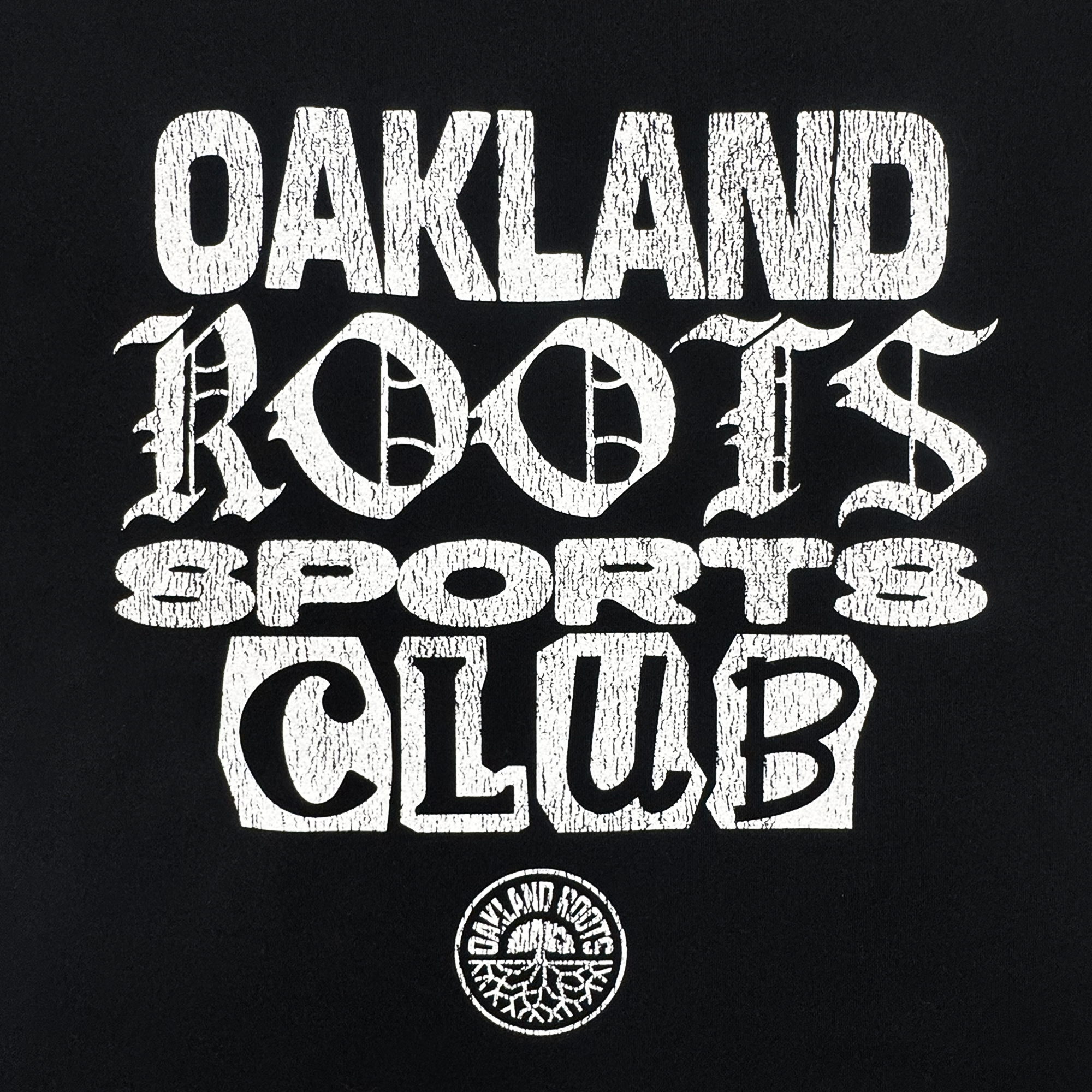 The Multi Text SS Tee by Oakland Roots SC features bold, stylized white text reading “OAKLAND ROOTS SPORTS CLUB” on a black background, above a circular Oakland Roots logo with the club name and signature tree graphic.
