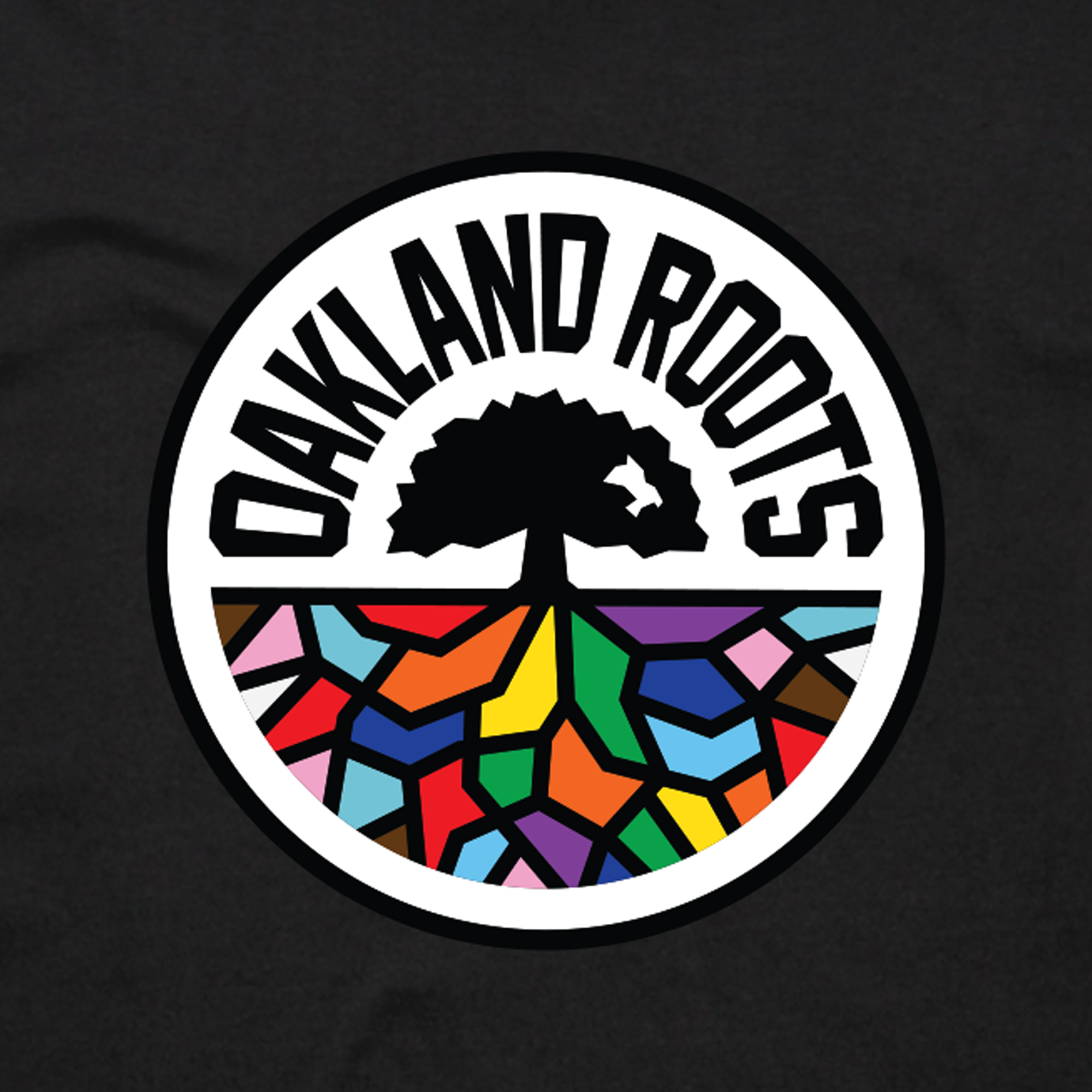 The image displays the Oakland Roots SC Pride Classic Tee, perfectly printed in men's sizing. This classic fit t-shirt, made from 100% cotton by Oakland Roots SC, features a circular design encased in a black border. At the top center is a black tree with thick, spreading branches. Below the tree, a colorful mosaic pattern forms the ground. The words "OAKLAND ROOTS" arc around it.