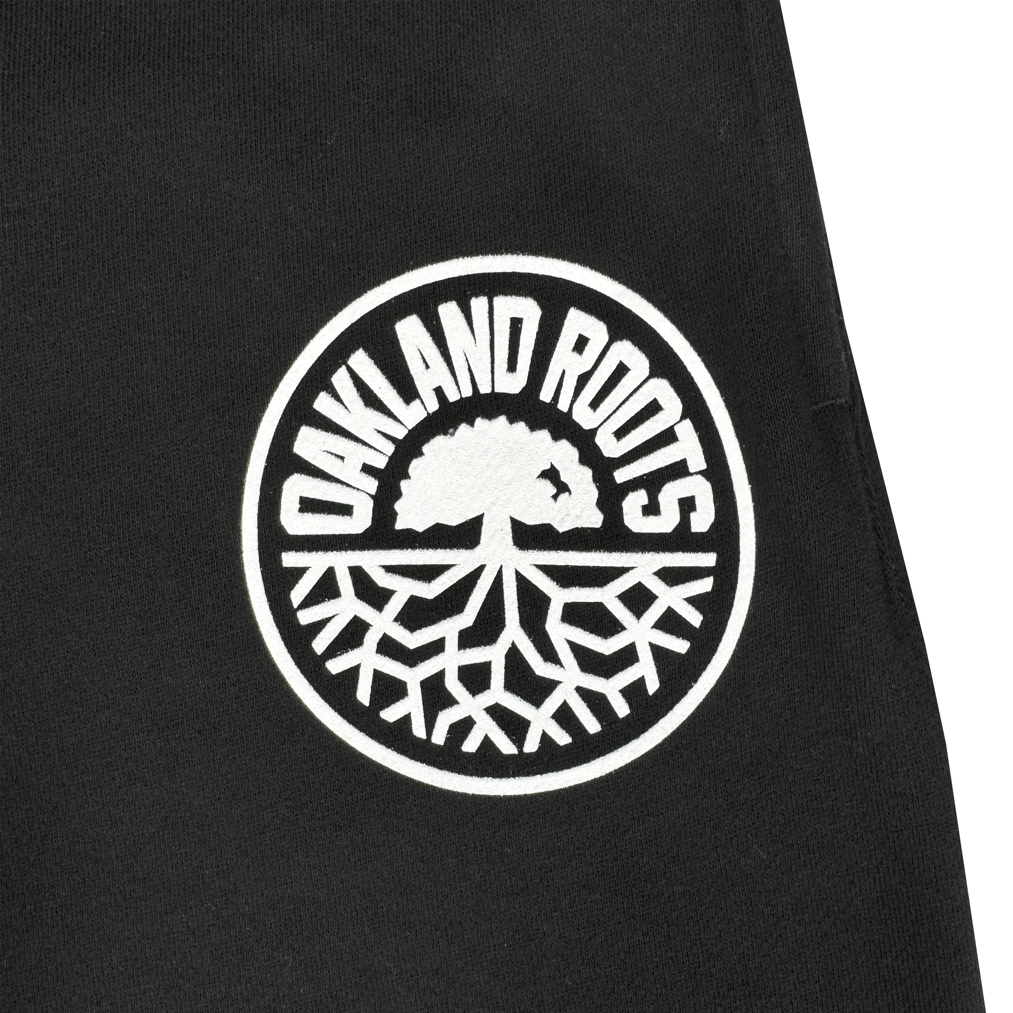 The Oakland Roots SC University Pant features black fabric with a white circular patch showing "OAKLAND ROOTS" above a stylized tree, symbolizing team pride, unity, and growth. Official gear by Oakland Roots SC.