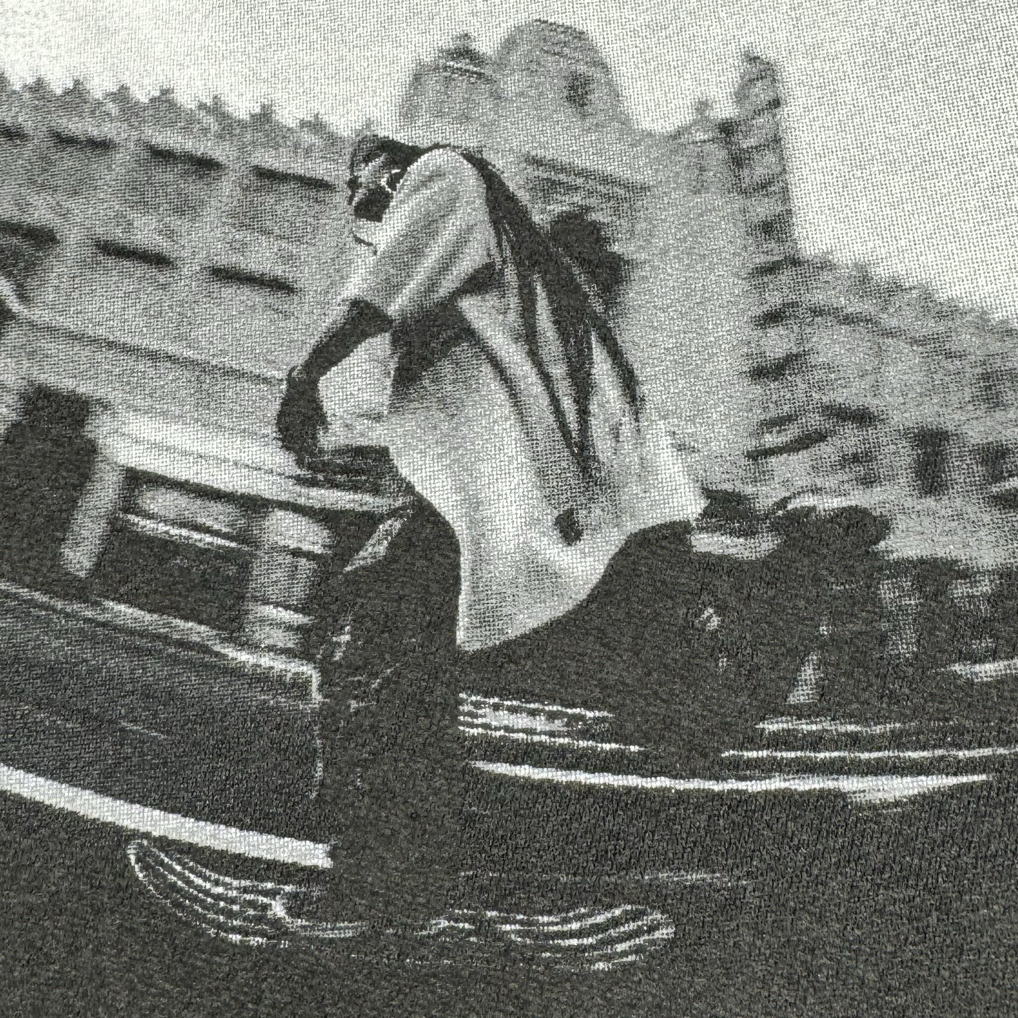 In the black and white photography, a skateboarder with long dreadlocks zips through the lively streets of Oakland, wearing the "Skateboarding is Beautiful Tee" by Oaklandish. The scene is highlighted by a vintage-style building with ornate architecture in the background, while motion blur enhances the sense of speed and movement, perfectly capturing an urban and dynamic atmosphere.