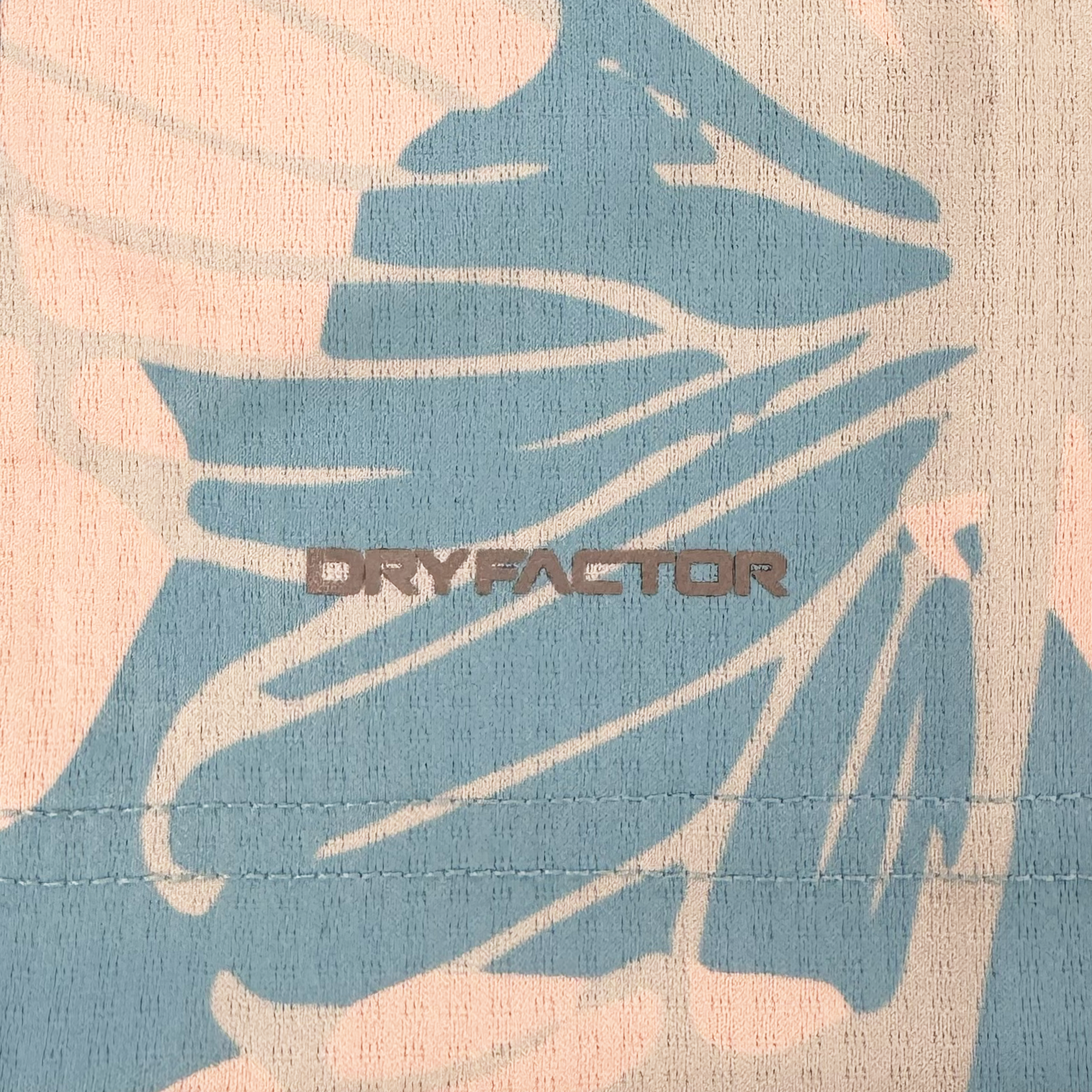 Close-up of Oakland Soul fabric from the Unisex Butterfly Effect Kit, with tan and muted teal abstract pattern, "DRYFACTOR" in bold lettering, a horizontal stitch line below, and ribbed texture inspired by Oakland Roots.