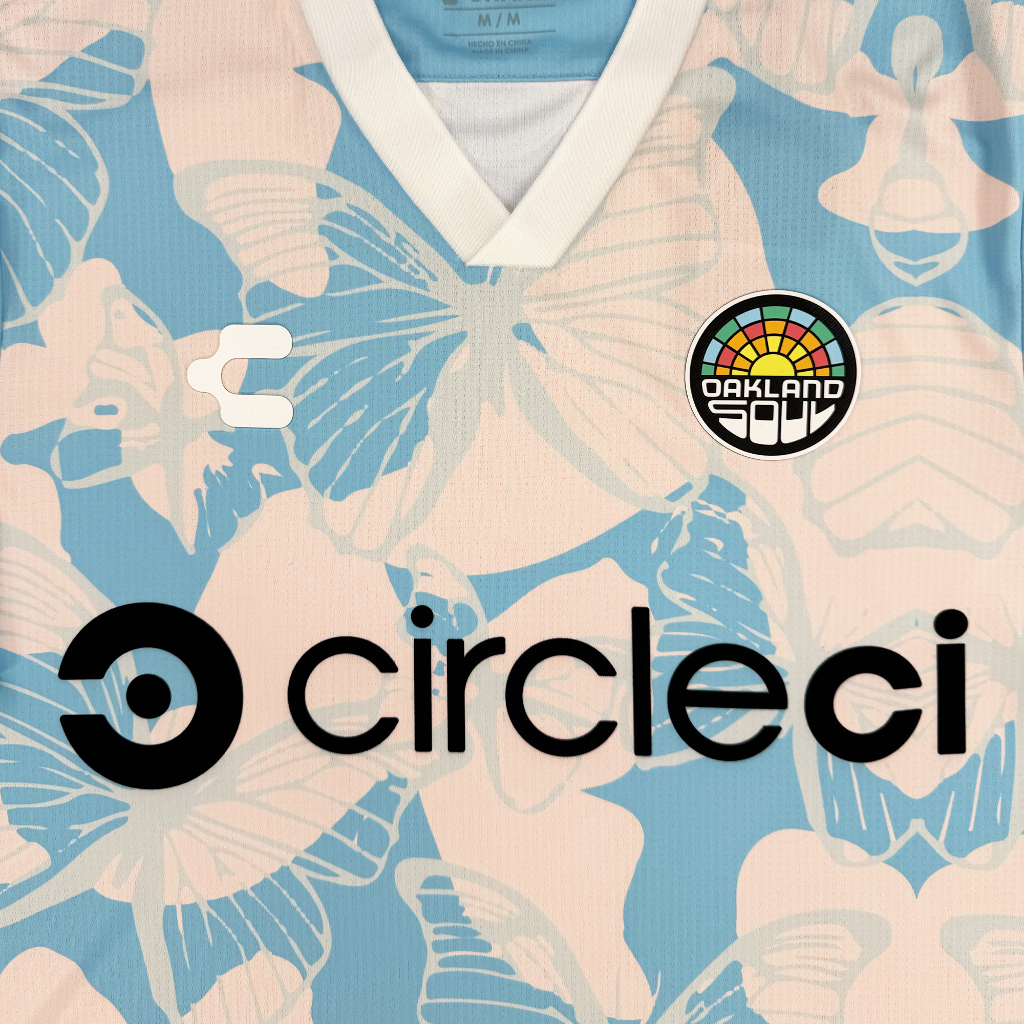 The Unisex Butterfly Effect Kit by Oakland Soul features a pastel pink and blue butterfly pattern, white V-neck collar and sleeve trim, plus three chest logos: Oakland Soul badge, stylized 'C', and bold black "circleci" sponsor logo.