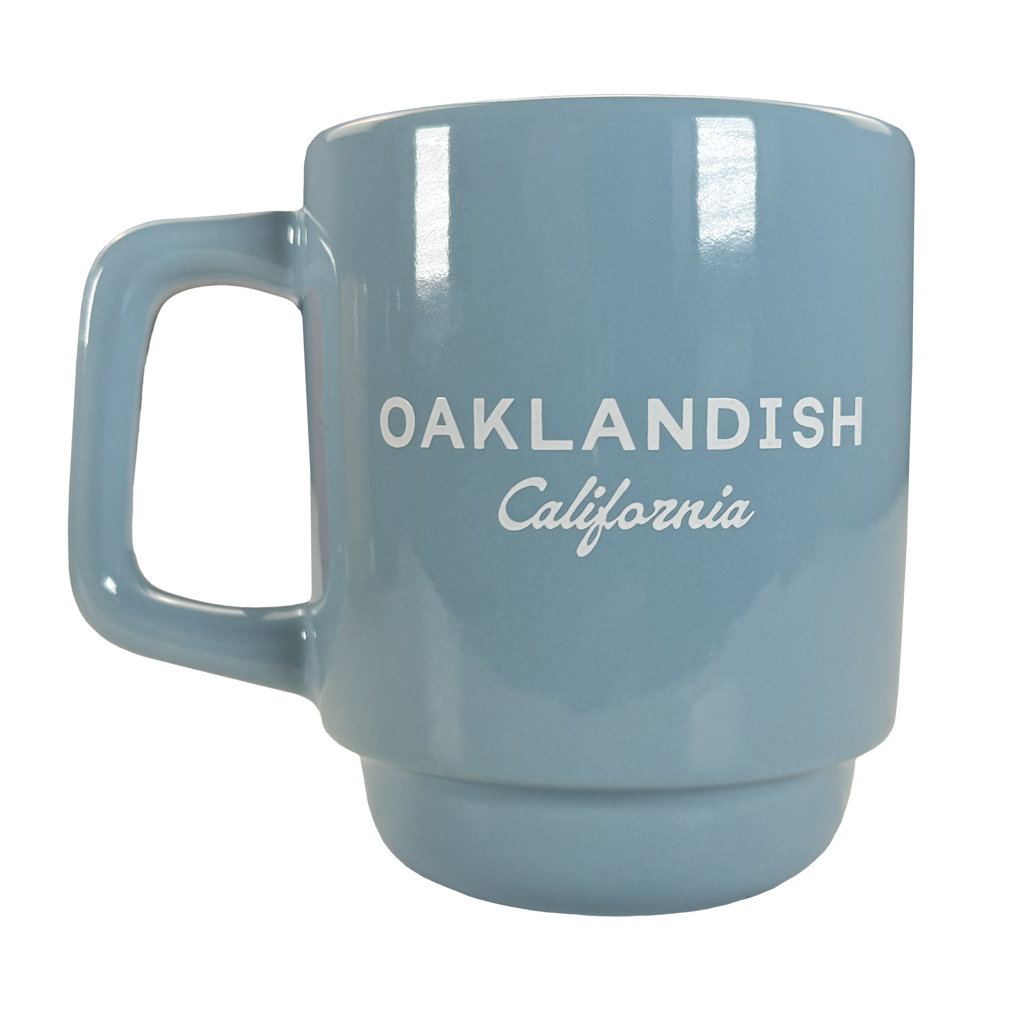 The Oaklandish Logo Stack Mug is a light blue ceramic mug with a squared handle, glossy finish, and white "OAKLANDISH California" text. This stackable drinkware piece is shown on a plain white background.