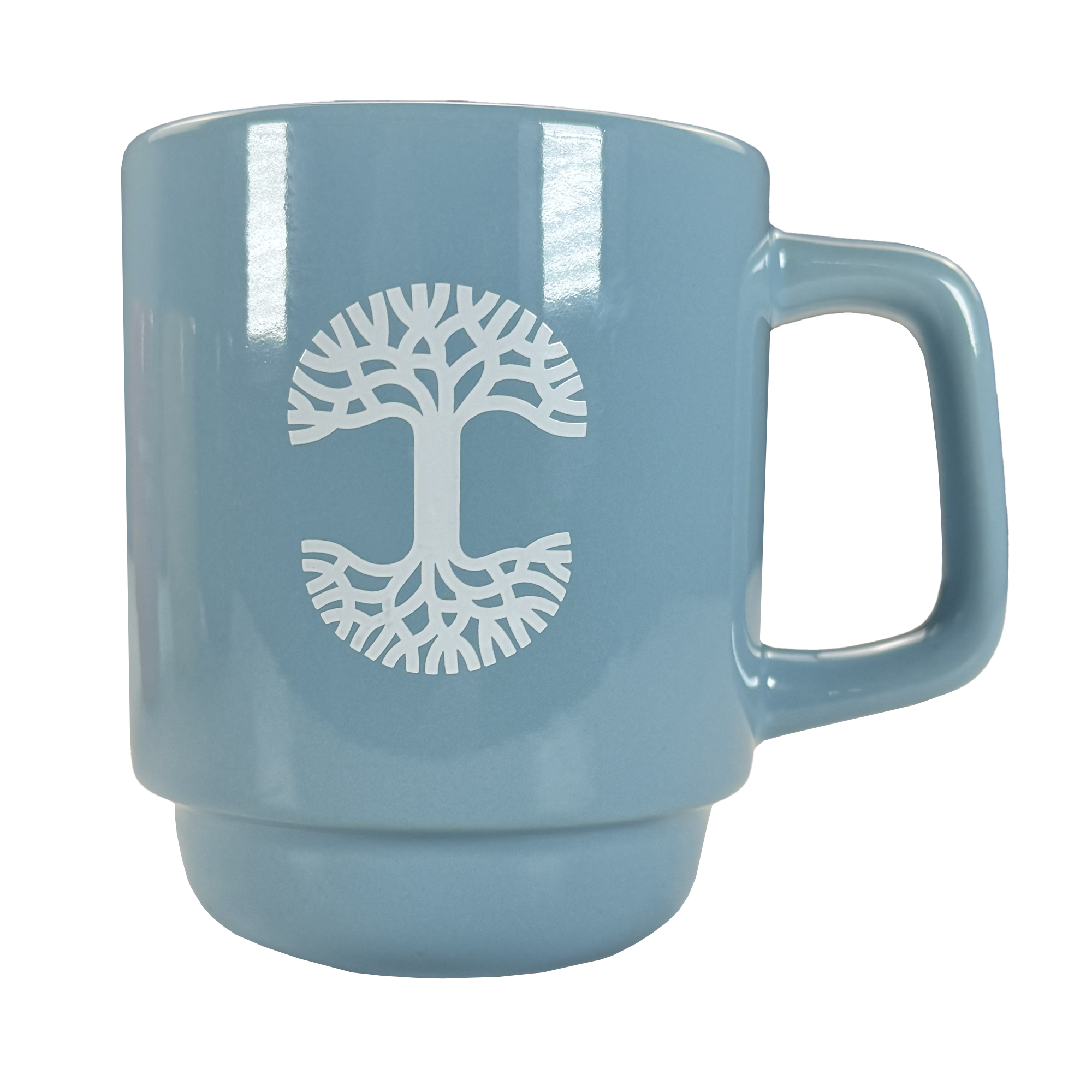The Oaklandish Logo Stack Mug is a light blue ceramic mug with a large handle, featuring a white stylized tree logo with symmetrical branches and roots. It is photographed against a plain white background.