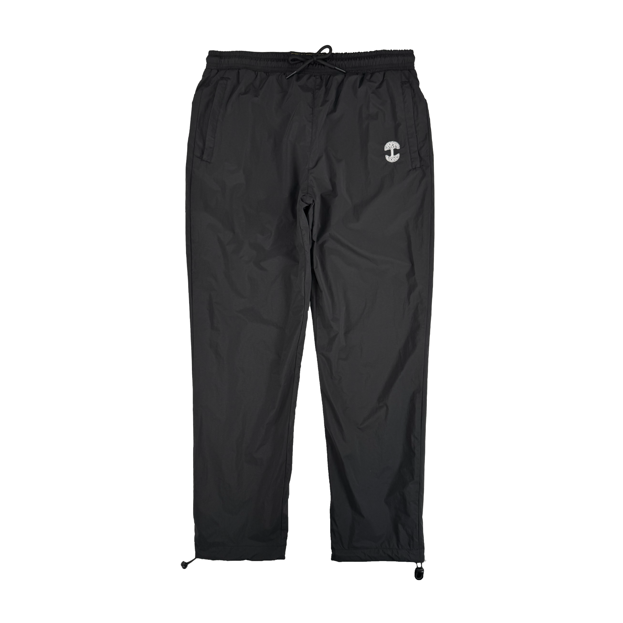The Oaklandish Susurrus Track Bottom is a pair of black nylon pants featuring an adjustable waistband, drawstring cuffs, two side pockets, and a small white circular logo on the left thigh. Set against a plain white background.