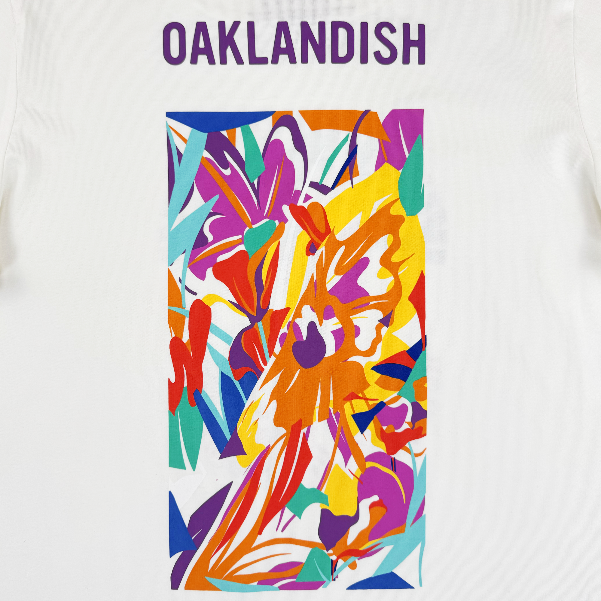 The Urban Tropics Tee by Oaklandish features “OAKLANDISH” in bold purple letters above a vibrant abstract design inspired by Kalani Ware, with colorful overlapping shapes for an energetic look.