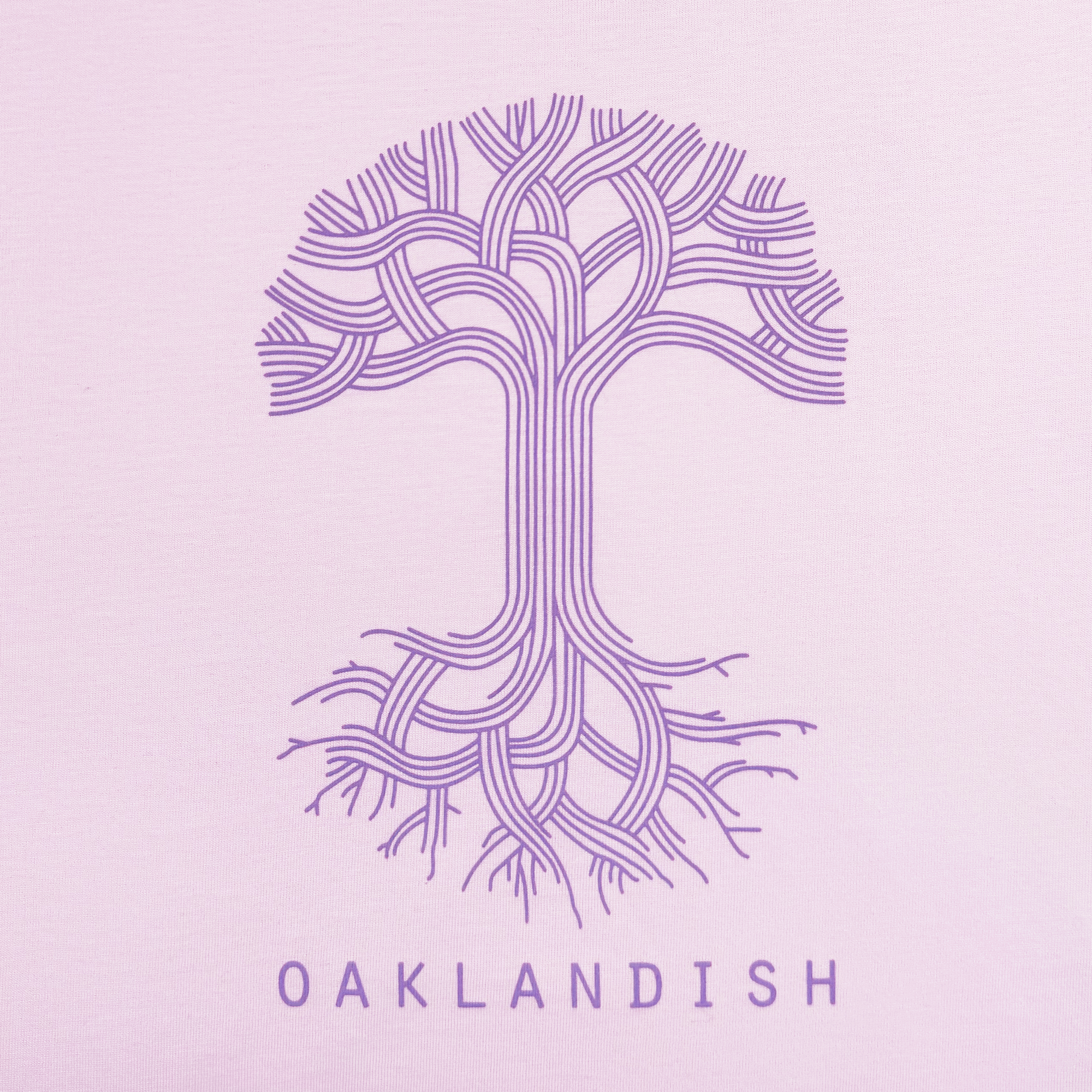 This light pink, 100% cotton Women's Oaklandish Classic Logo Tee features a purple tree with a lattice-like trunk and branches. "OAKLANDISH" appears below, symbolizing growth and connection, offering a timeless addition to your wardrobe.