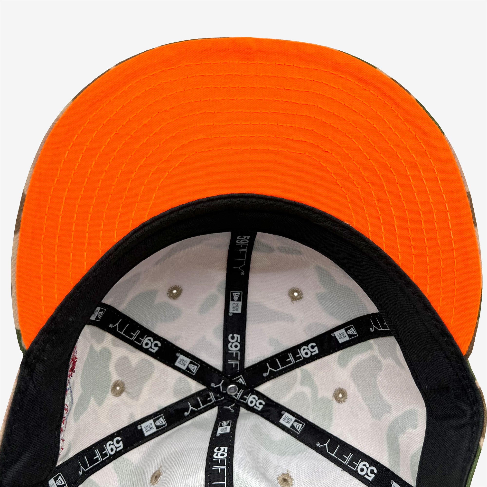 The underside of the New Era Oakland A's 59FIFTY Fitted Cap features a brim with vibrant orange and neatly stitched lines. The inner section showcases a Duck Camo pattern, complemented by black fabric strips labeled "59FIFTY New Era." Metal rivets are also visible, ensuring proper ventilation. The background is plain white.