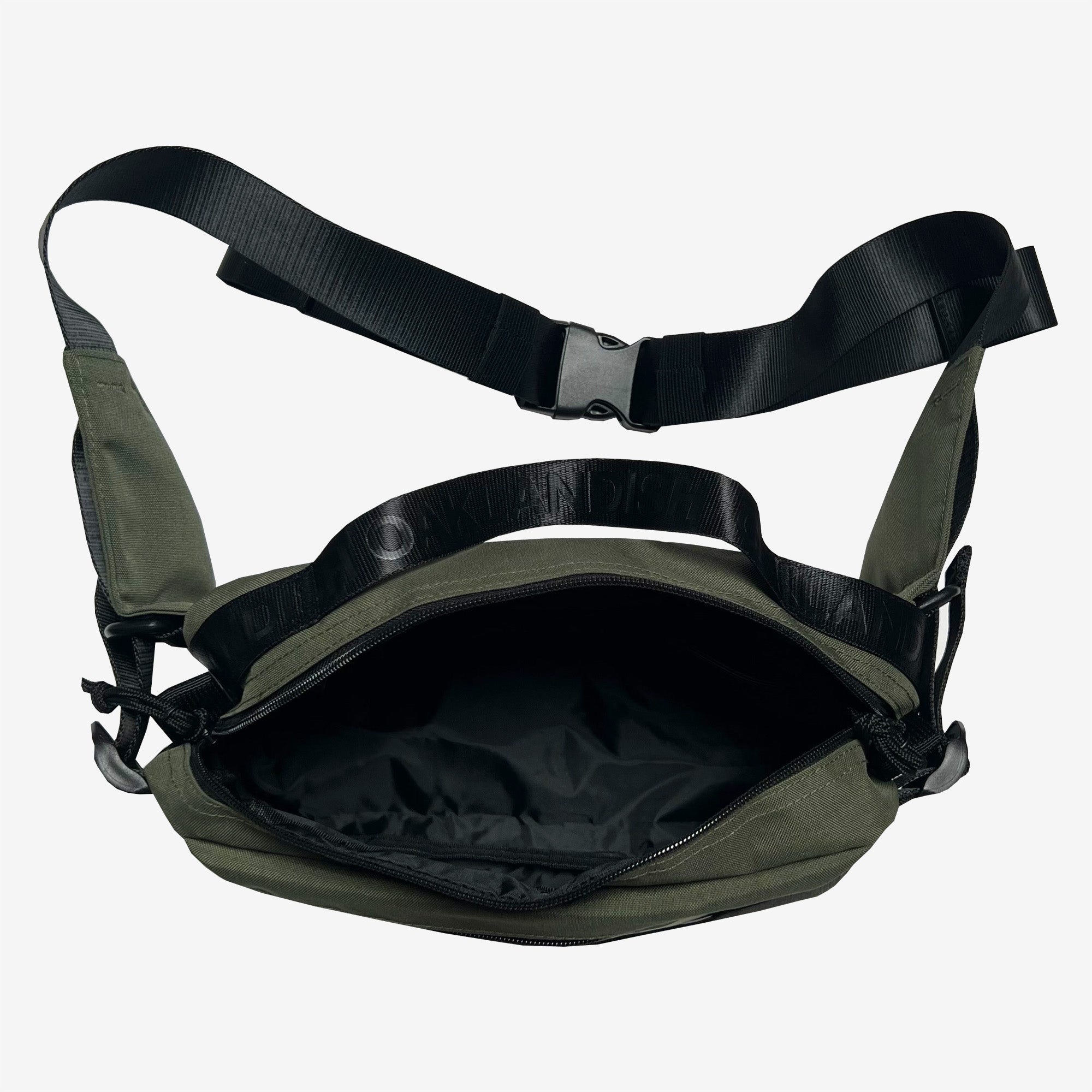 The Oaklandish Hip Bag is a green unisex crossbody bag featuring a black adjustable shoulder strap and a large buckle clasp. The bag is shown open, revealing a spacious, unlined black interior. Two small black side loops are near the base of the strap, providing options for additional attachment or accessories. The background is plain white.