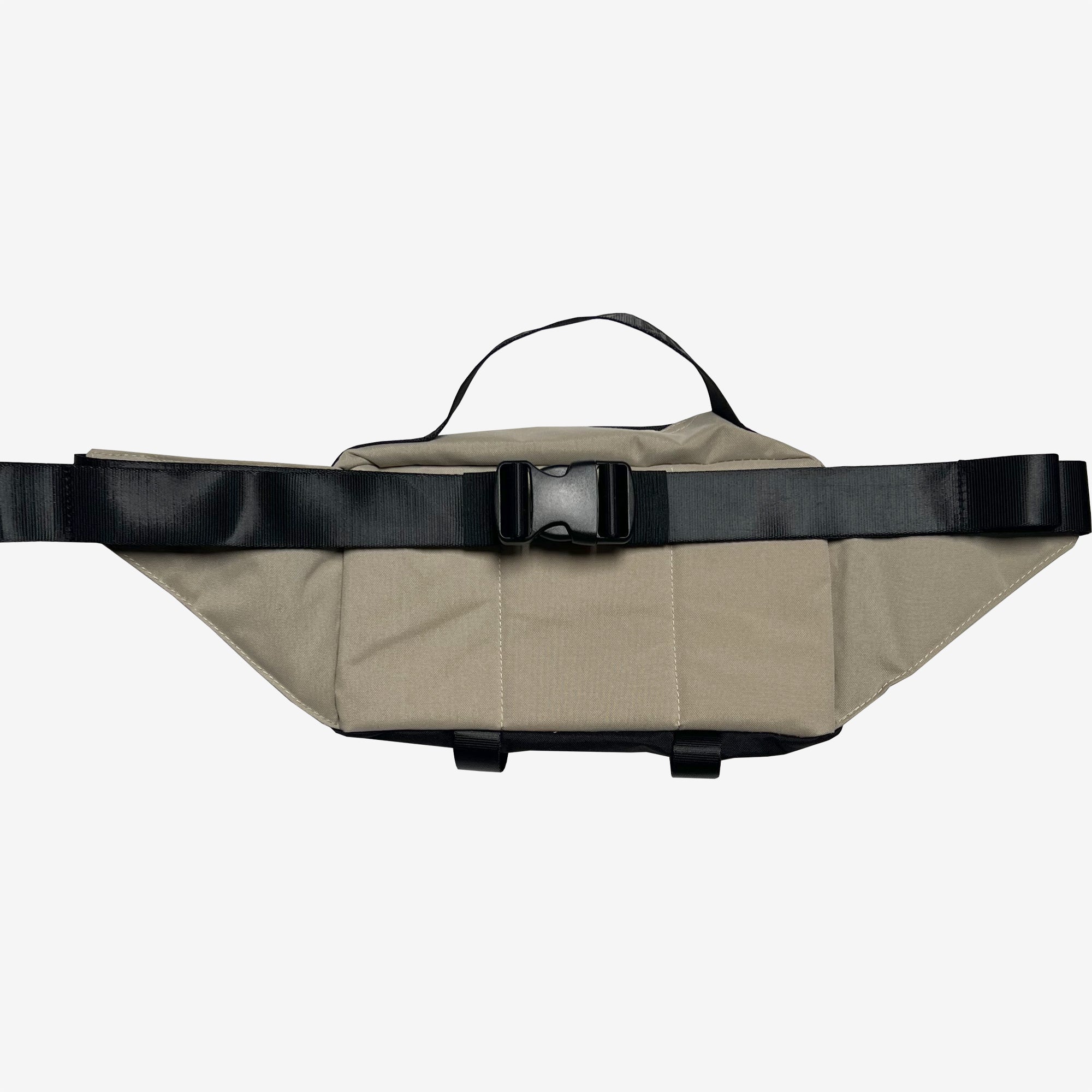 The Oaklandish Hip Bag by Oaklandish is a beige-colored sling pack that features a large black buckle and adjustable black straps. It has a minimalist design with a small carrying handle on top and appears to be made from sturdy, durable fabric. The bag is showcased against a plain, light grey background.