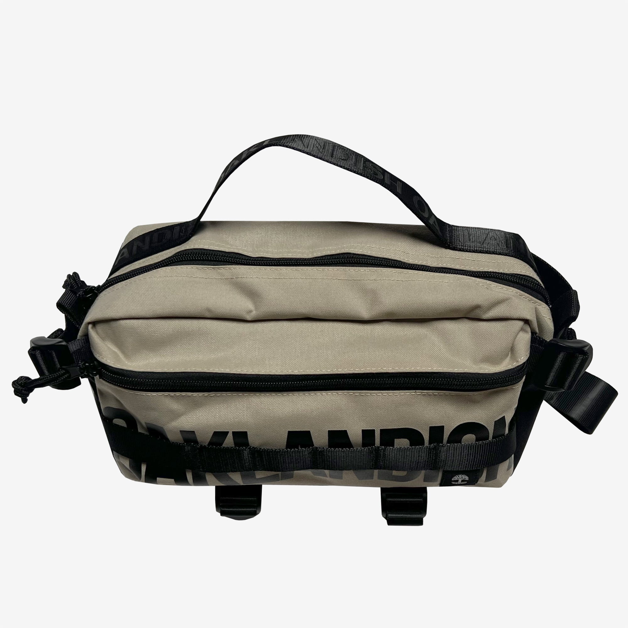 Introducing the Oaklandish Hip Bag by Oaklandish, a khaki-colored sling pack featuring black zippers and adjustable straps. This versatile hip/shoulder bag includes multiple compartments, such as a main zipper pocket and a smaller front zipper pocket. Black lettering is visible on both the front and back of the bag, while the strap is equipped with sturdy black buckle fastenings.