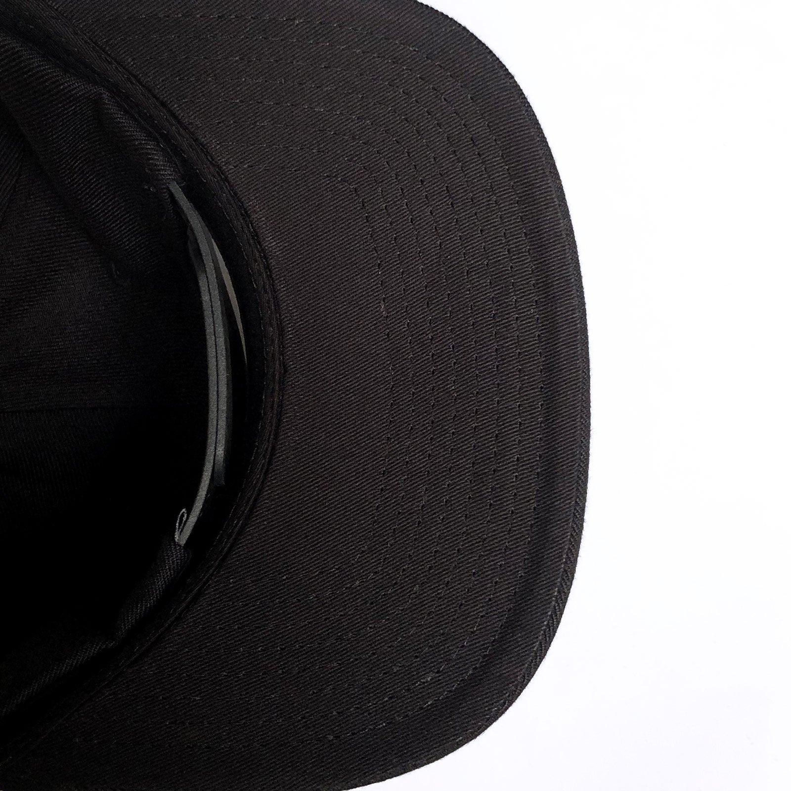 A close-up view of the Hieroglyphics Hiero Crew Snapback, a black baseball cap, positioned with its brim facing the top-right corner of the image. The stitching details are visible on the brim, and the inner band and part of the crown are shown in shadow. The background is plain white, contrasting with the dark color of the cap.
