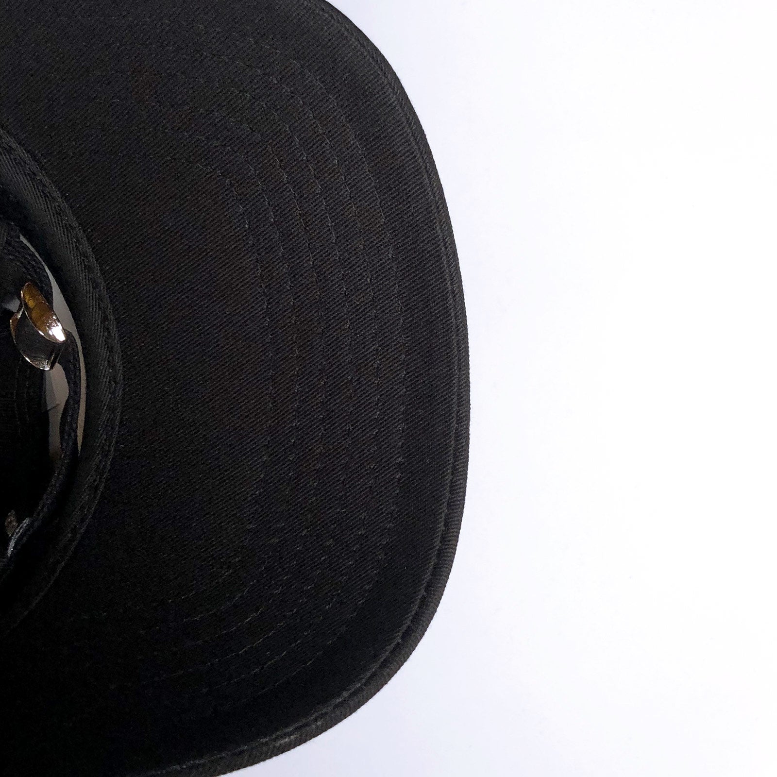 A close-up of the brim and part of the crown of the Hiero Crew Dad Hat by Hieroglyphics. The black cap features a textured fabric with visible stitching details on the brim, accented by an adjustable strapback. The background is a plain, light-colored surface. The photo is cropped so that only a portion of the hat is visible on the left side.