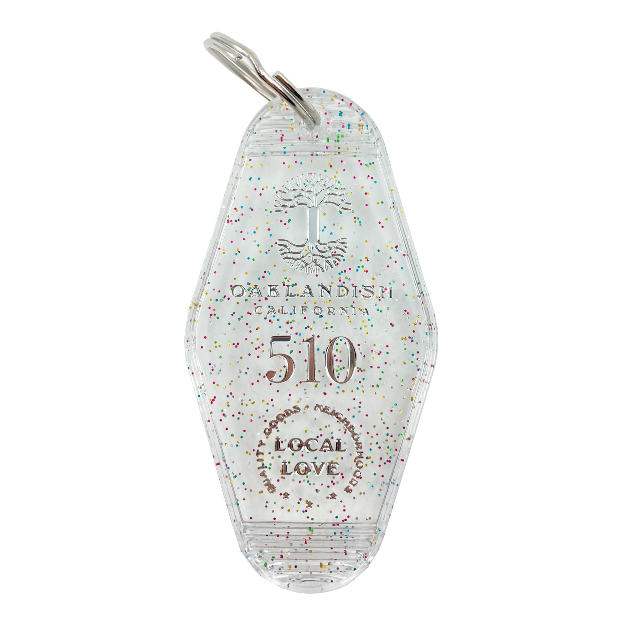 The Local Love Key Tag by Oaklandish is a transparent keychain shaped like a vintage motel key tag, featuring multicolored speckles and a small key ring attached at the top. It is engraved with "OAKLANDISH, CALIFORNIA," a tree logo, the number "510," a dotted semicircle, and the words, "LOCAL LOVE." Perfect for accessories enthusiasts.