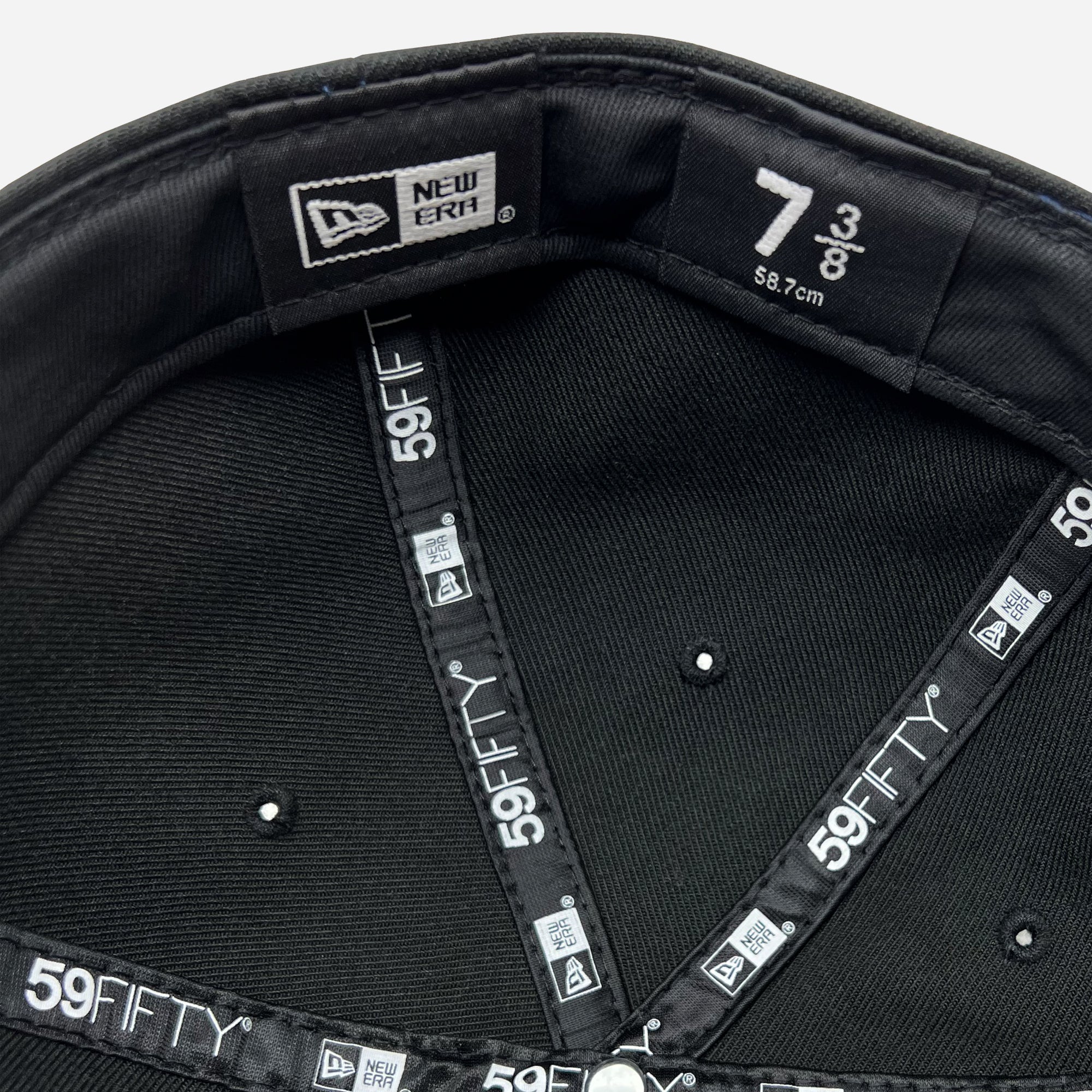 The image shows the inside of a black New Era Official 59FIFTY Fitted Cap by Oaklandish. It features a size tag reading "7 3/8," which corresponds to 58.7 cm, as well as multiple "New Era" and "59FIFTY" logos on the inner lining and seam tapes. The interior details, stitching, and distinctive Oaklandish style are all prominently visible.