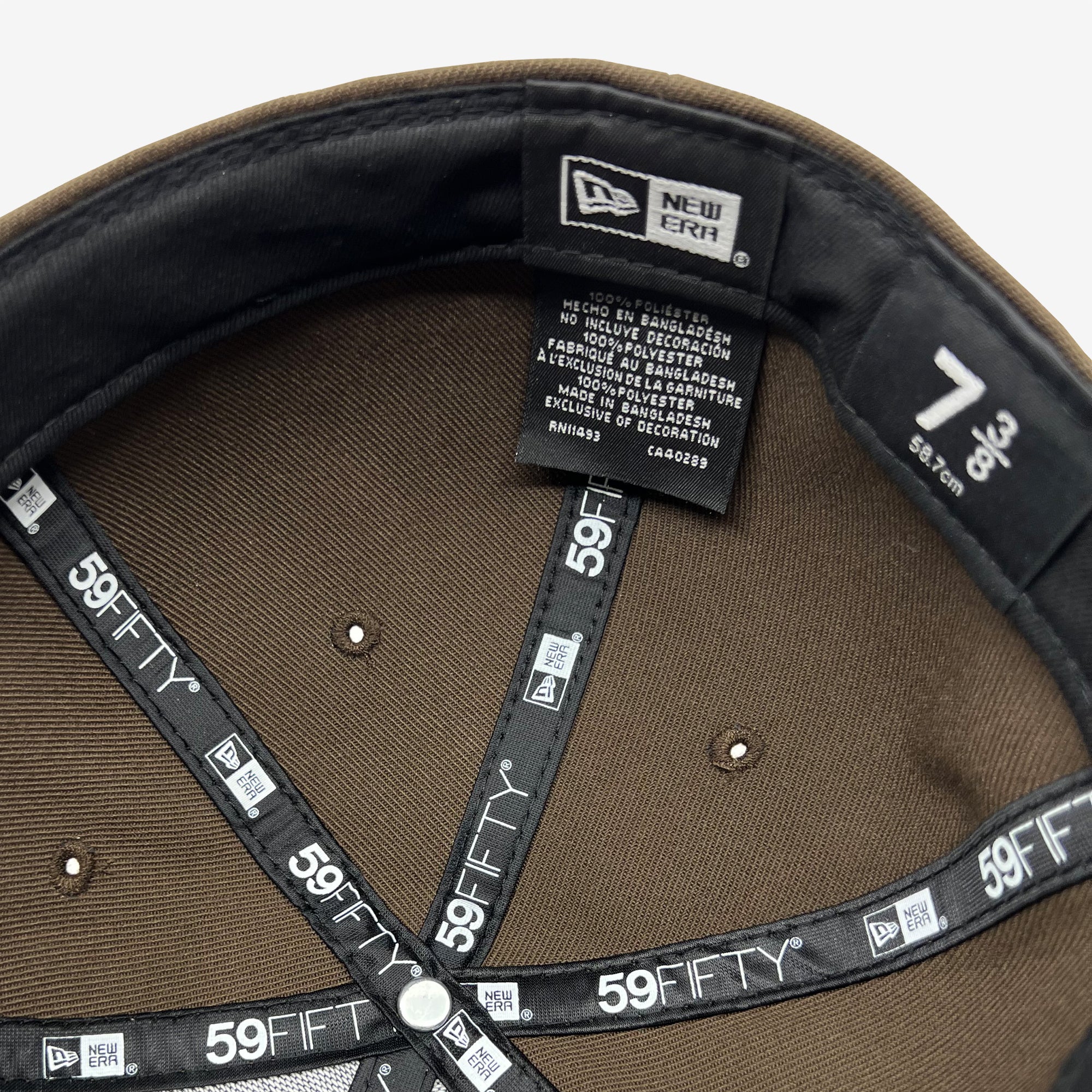 Interior view of the New Era Official 59FIFTY Fitted Cap by Oaklandish, size 7 3/8. The label inside displays care instructions and material composition in multiple languages. The inner band highlights branding such as the New Era logo, "59FIFTY," and Oaklandish. Small air holes are also visible on this headwear.