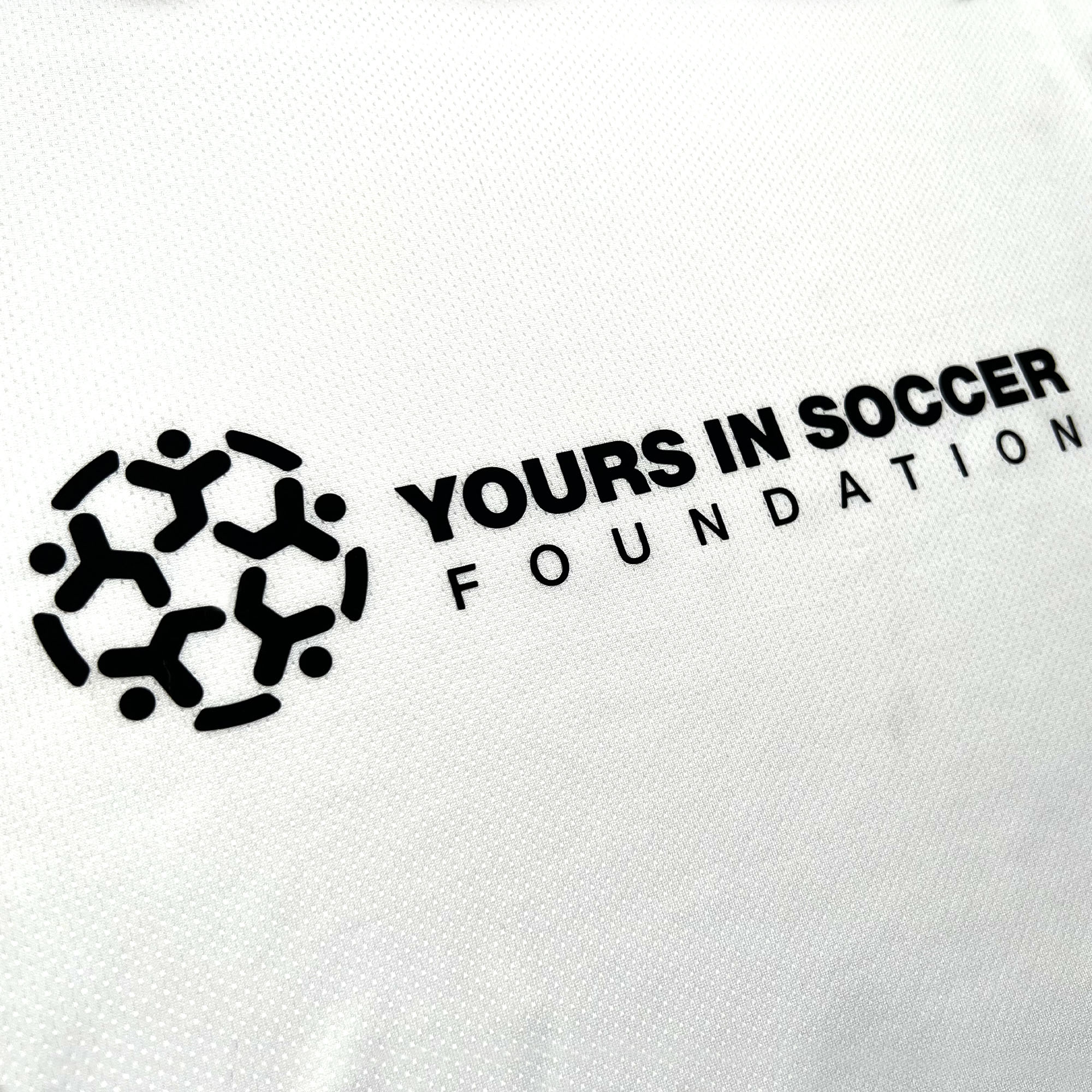 The image shows the logo of the "Yours in Soccer Foundation," a nonprofit organization, on the Oakland Genesis Home White product from Partner. The logo features black stylized human figures arranged in a circular formation, resembling a soccer ball. To the right of the graphic, the organization's name is written in bold, black text.