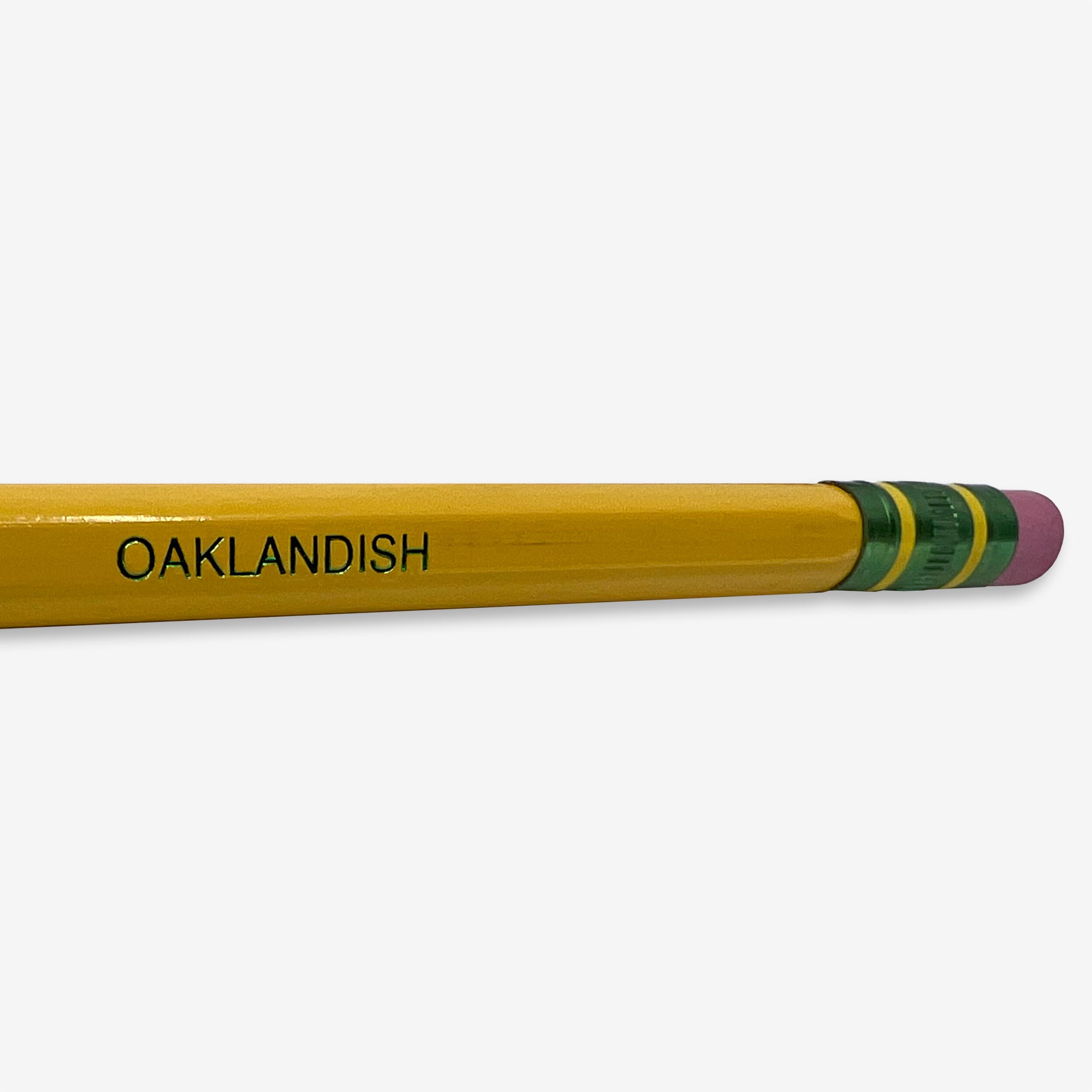 An Oaklandish Pencil Dixon Ticonderoga No. 2, renowned for its extra smooth writing, lies horizontally on a white surface. The word "OAKLANDISH" is printed in black letters near the pink, latex-free eraser, which is attached with a green and yellow metal band.