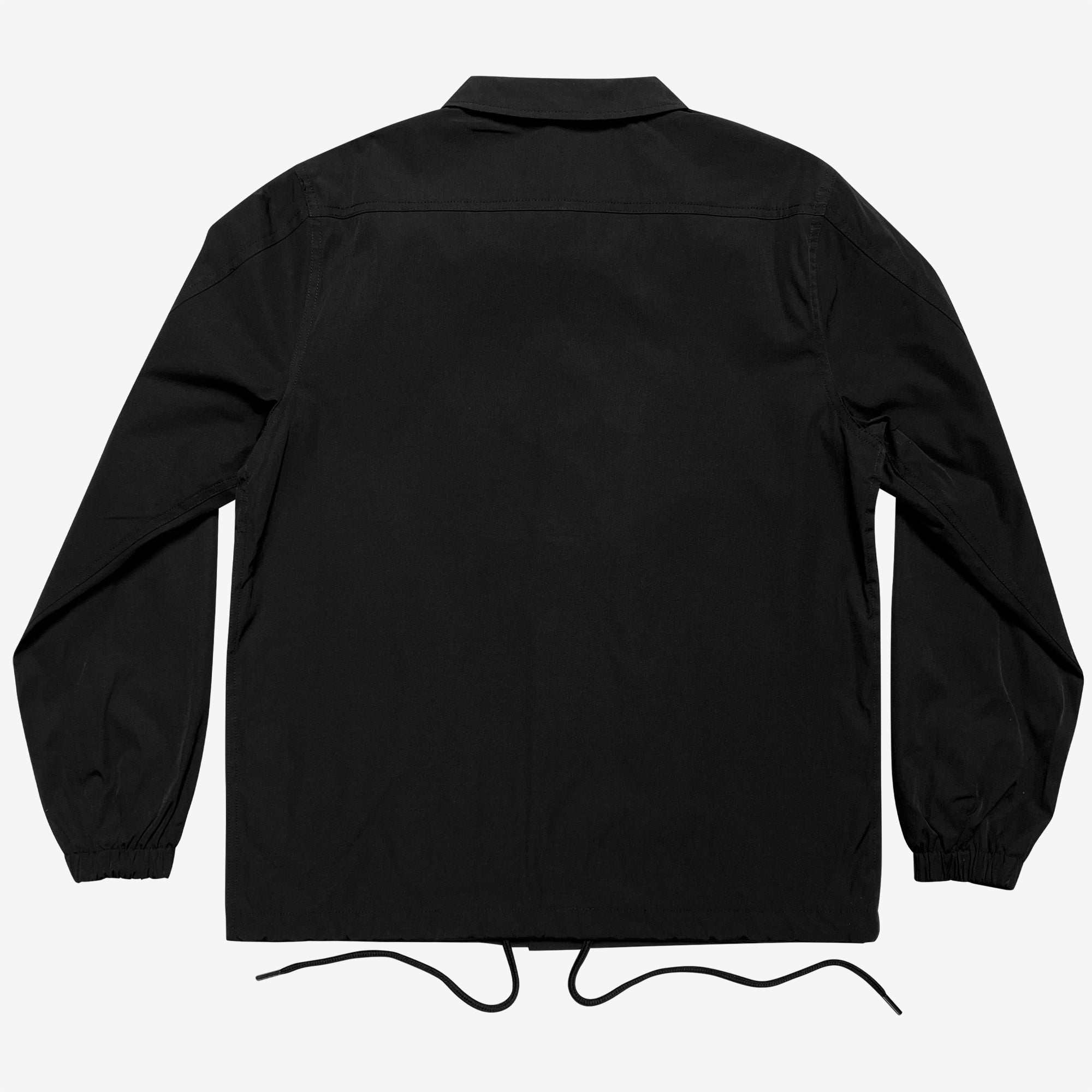 A black Oaklandish Premium Coaches Jacket is displayed from the back, showcasing long sleeves with elastic cuffs. The jacket features a minimalist design with a straight hem and a collar at the top. It is water-resistant and includes drawstrings hanging from the bottom hem for fit adjustment. The background is plain white.