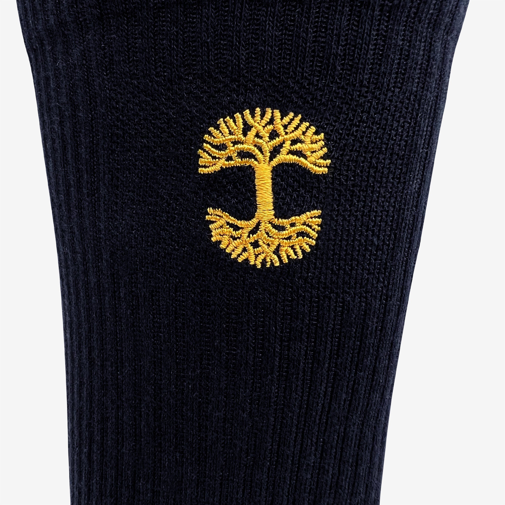 A close-up of the Embroidered Logo Sock by Oaklandish, featuring black and gold ribbed fabric and an intricate yellow tree with detailed roots and branches. The symmetrical design is centrally placed, creating a striking contrast against the dark background.