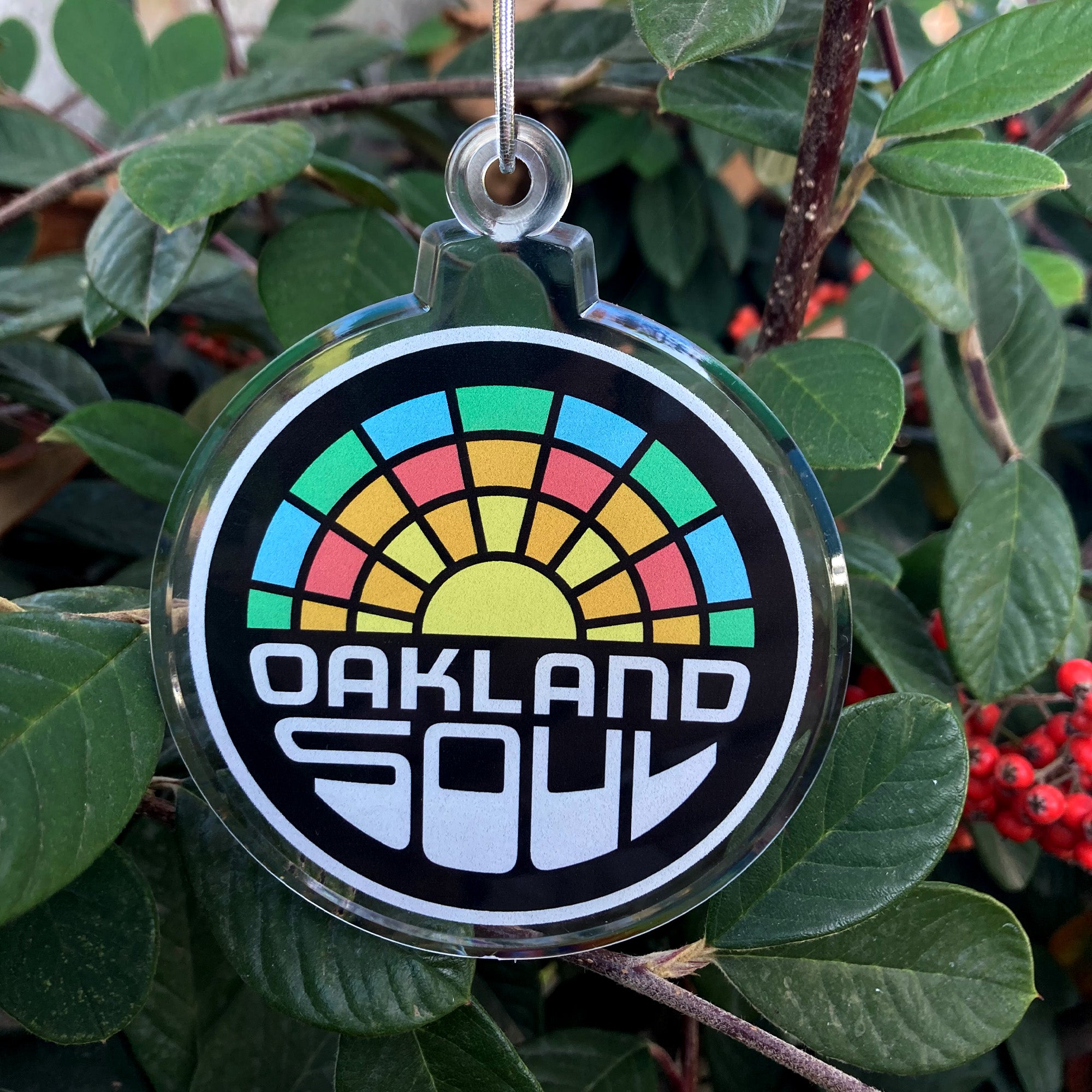 Full-color Oakland soul crest  on a holiday tree ornament with silver string hanging on a bush.