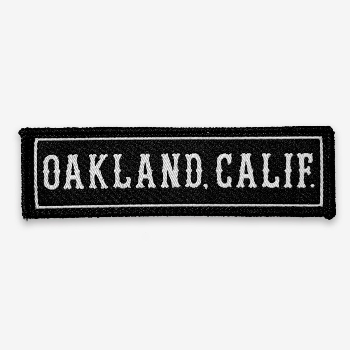 The Oaklandish "Oakland CA Patch" is a rectangular black iron-on patch featuring capital white text that reads, "OAKLAND, CALIF." The patch has a fabric texture and the text is surrounded by a white rectangular outline—perfectly pure Oakland accessories for any collection.