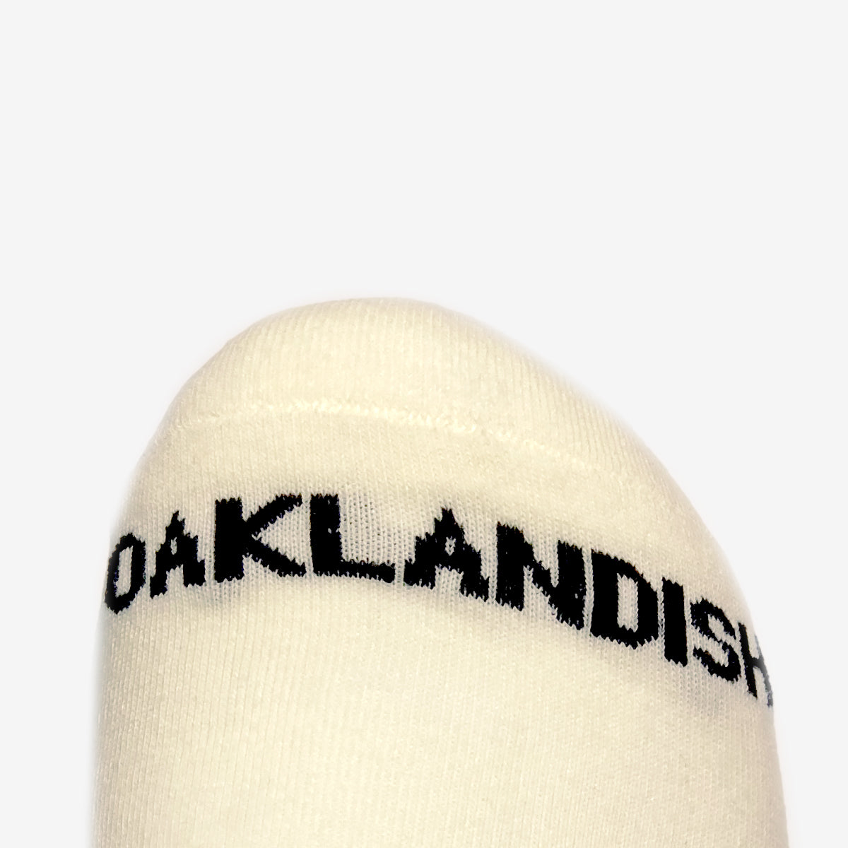 A close-up of the toe area of Embroidered Logo Socks from Oaklandish against a plain background. The word "OAKLANDISH" is printed in bold, black letters across the top, showcasing an embroidered logo. The stitching and fabric texture are clearly visible.