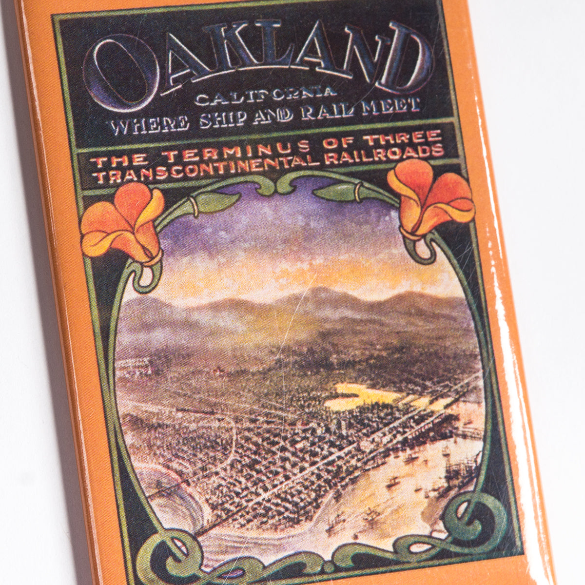 Introducing the "Poppies Magnet" by Oaklandish—a vintage-inspired keepsake featuring art deco embellishments that promote Oakland, California. Showcasing an eye-catching aerial illustration of the city and its port, accompanied by vibrant orange poppies, the magnet reads, "Oakland, California - Where Ship and Rail Meet - The Terminus of Three Transcontinental Railroads." Ideal as a memorable Oakland souvenir or a chic addition to your home accessories.